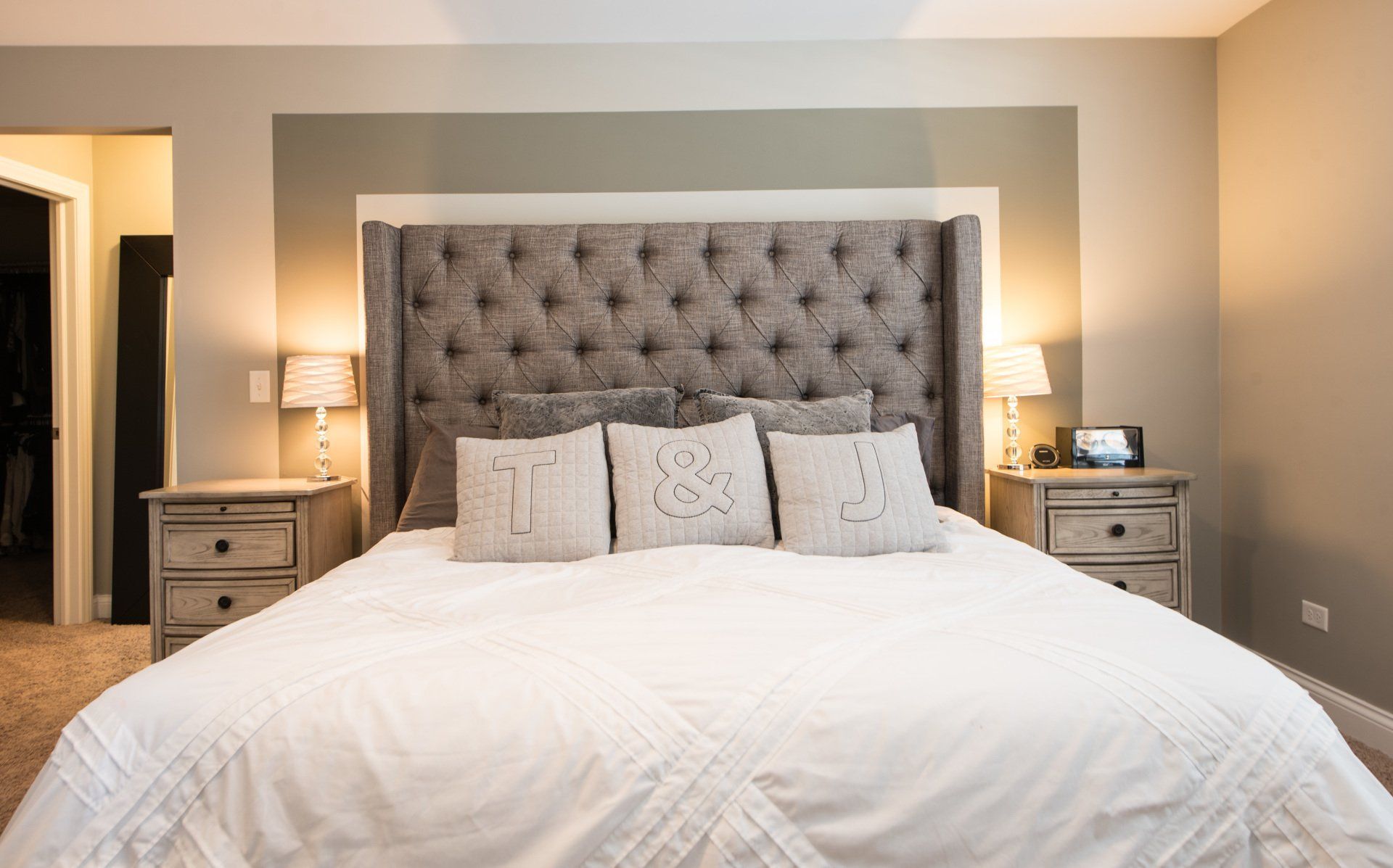 Bedroom with a tufted gray headboard, white bedding, and matching bedside lamps on either side.