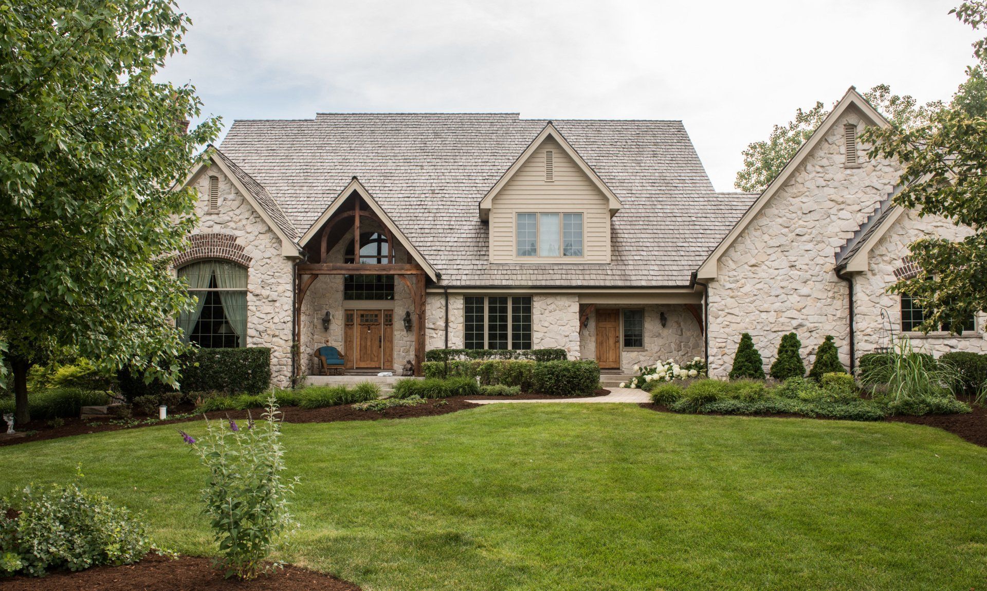 Stone suburban house with a gabled roof, front porch, and manicured green lawn