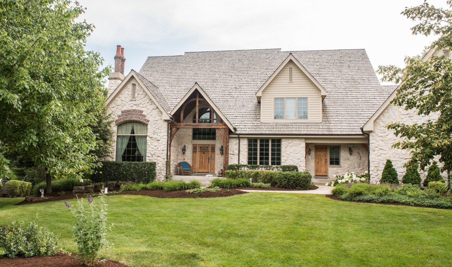 Stone cottage with a steep shingled roof, front garden, and manicured lawn in a leafy setting