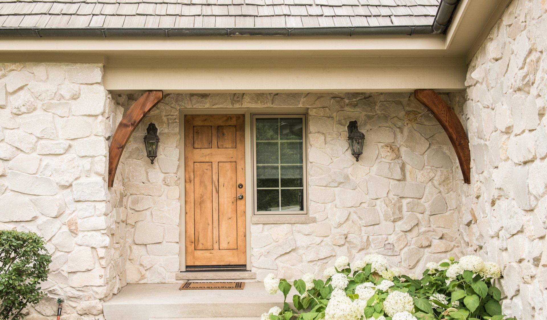 Stone house entrance with wooden door, small window, and white flowers by the step