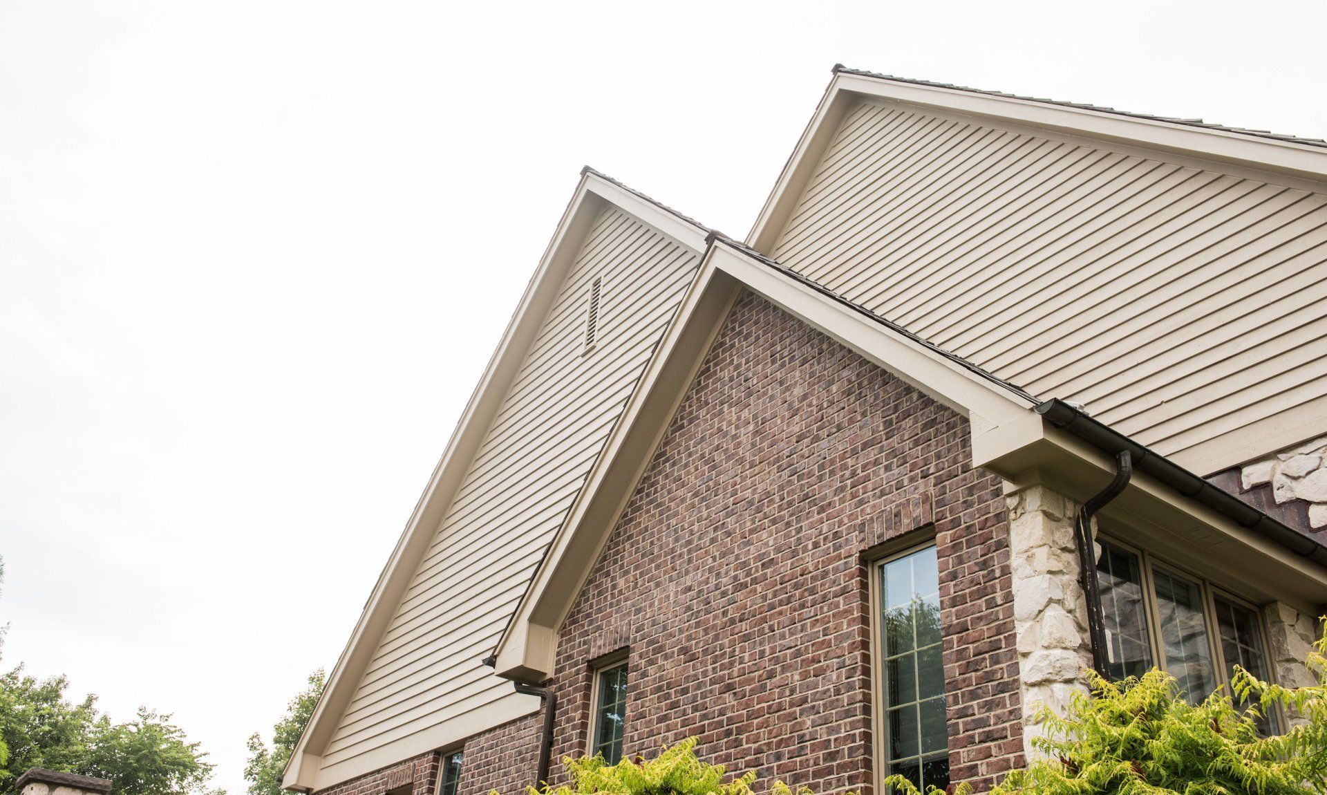 Close-up of a tan house roof and gable with brown brick siding and white trim.