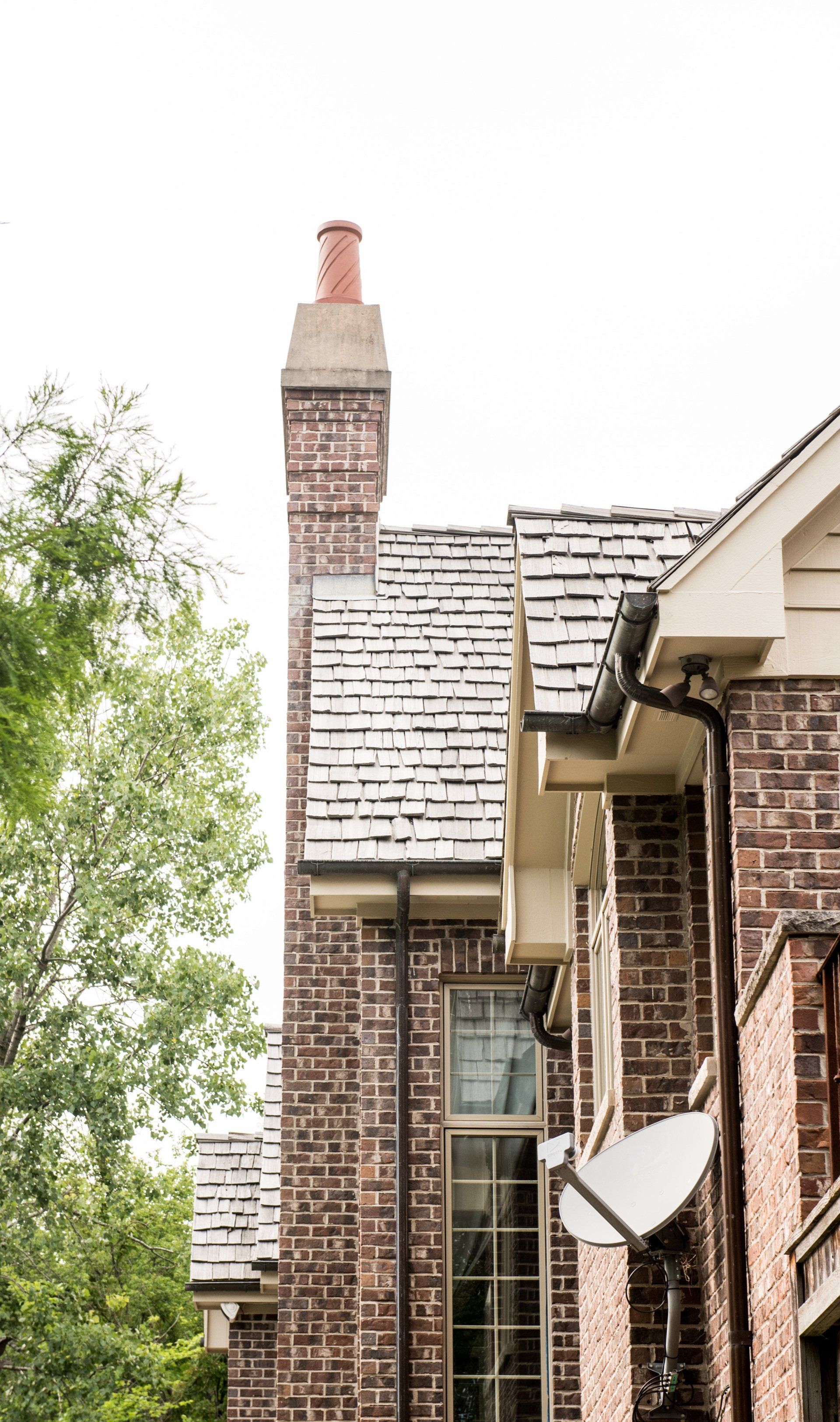 Brick townhouse exterior with white shingled roof, chimney, and a satellite dish near a tree