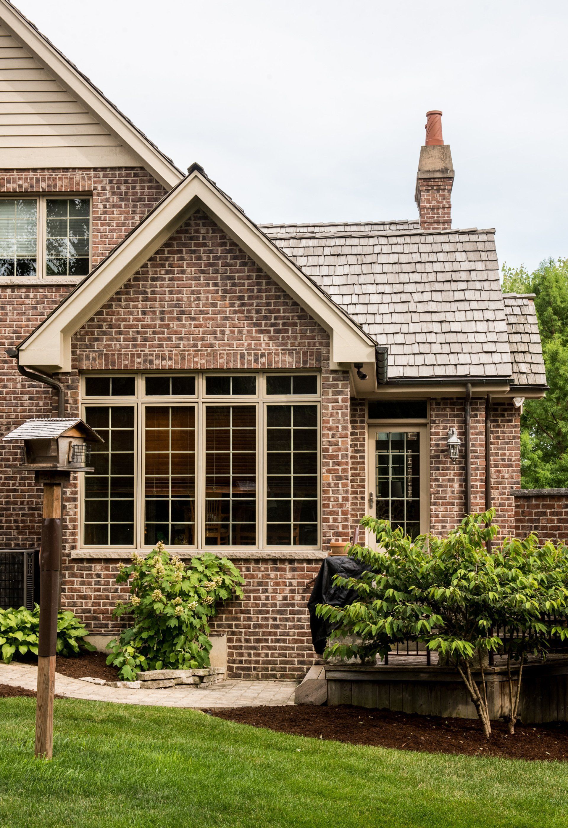 Brick suburban house exterior with beige roof, large front windows, and green lawn