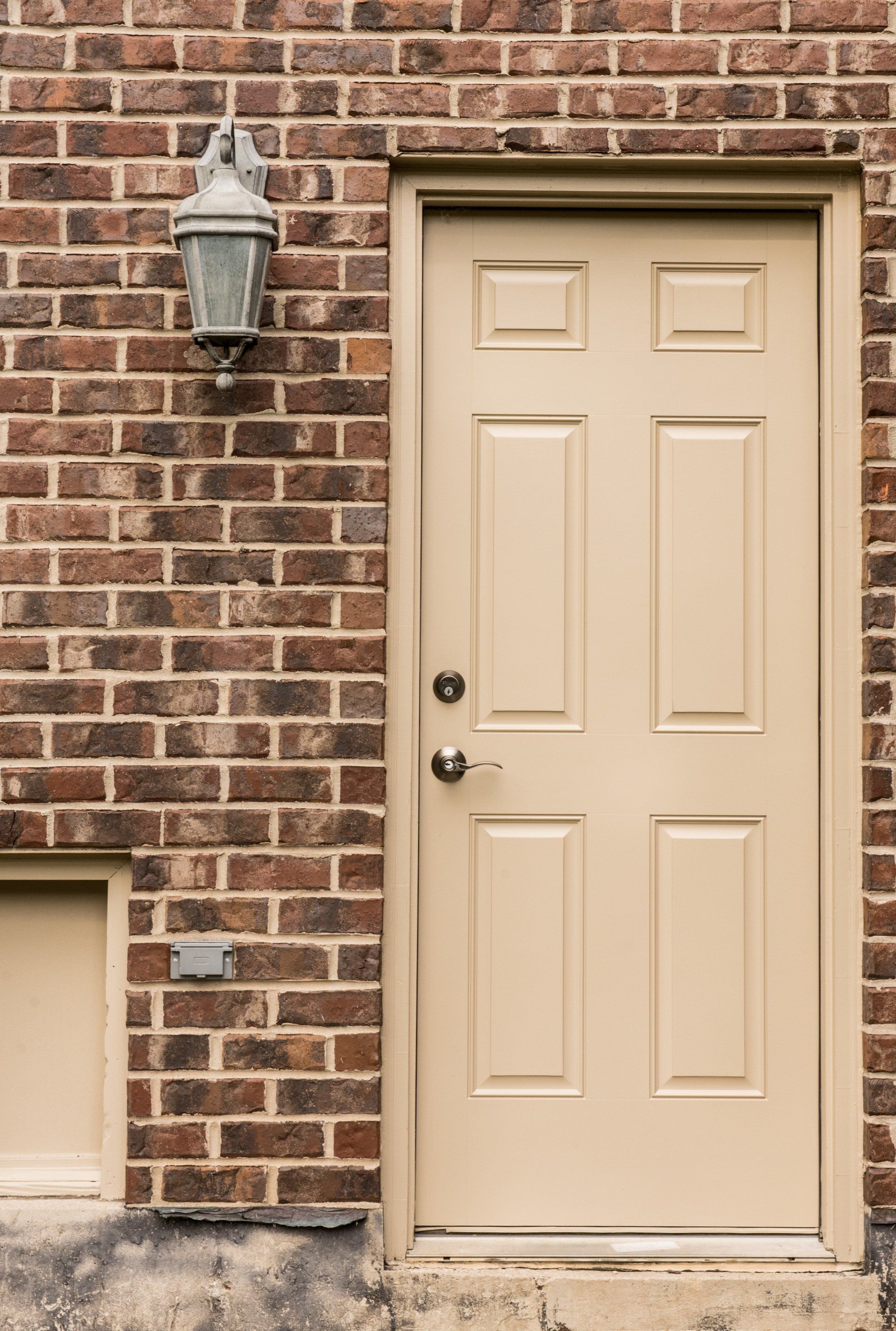 Beige front door set in a brick wall beside an outdoor lantern