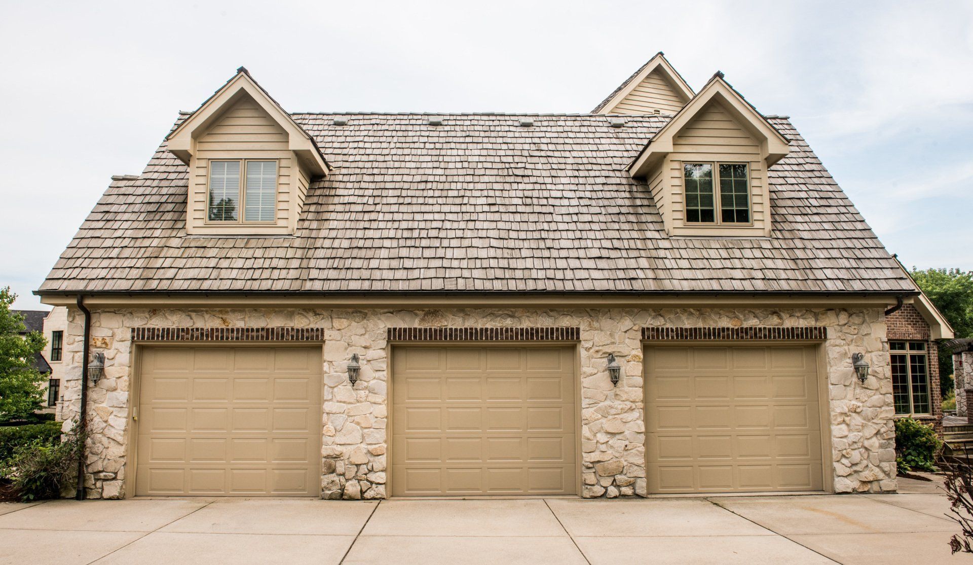 Three-car beige garage with stone house facade and dormer windows.