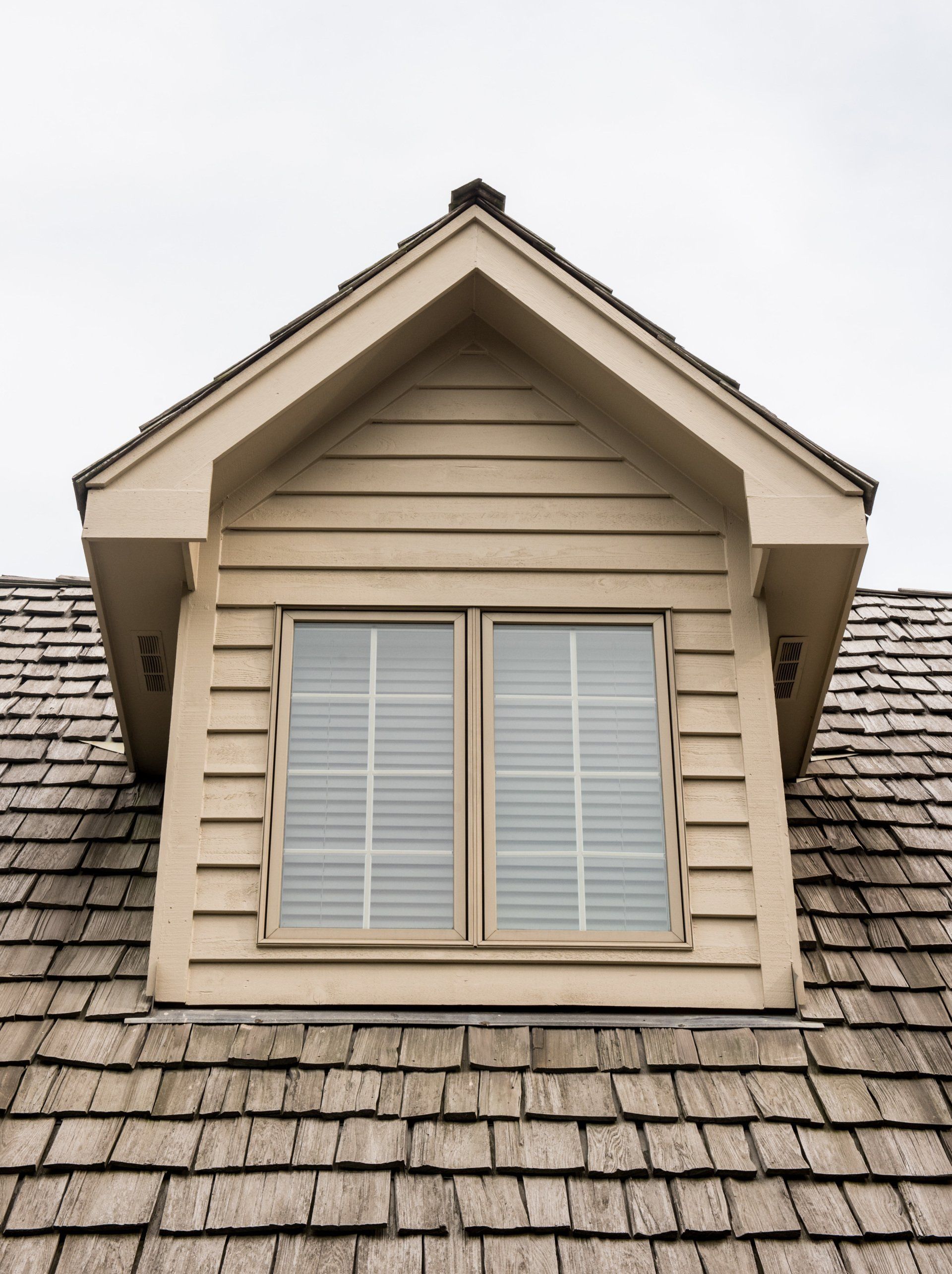 Dormer window with closed white shutters on a tan house roof