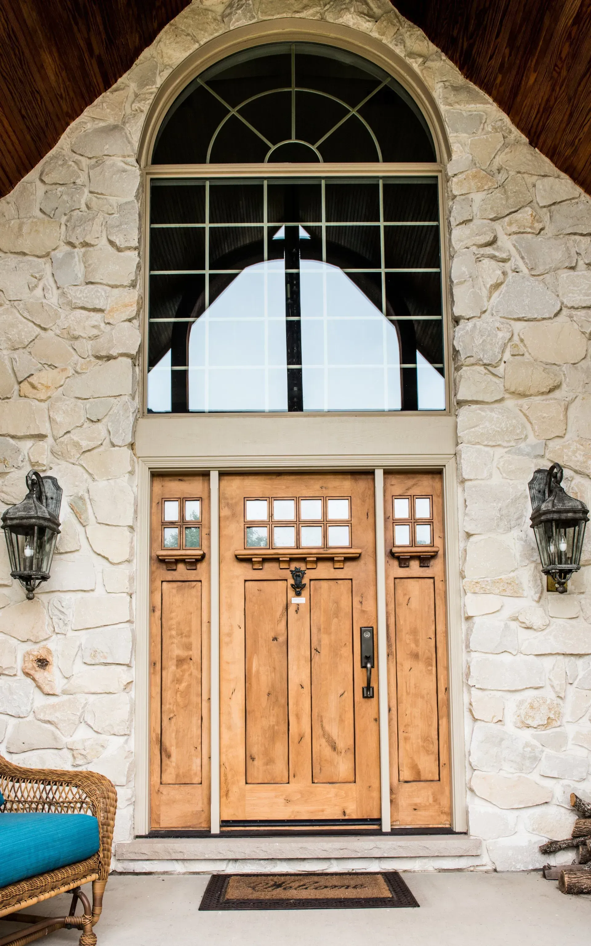 Stone house entrance with arched window, wooden double doors, and wall lanterns