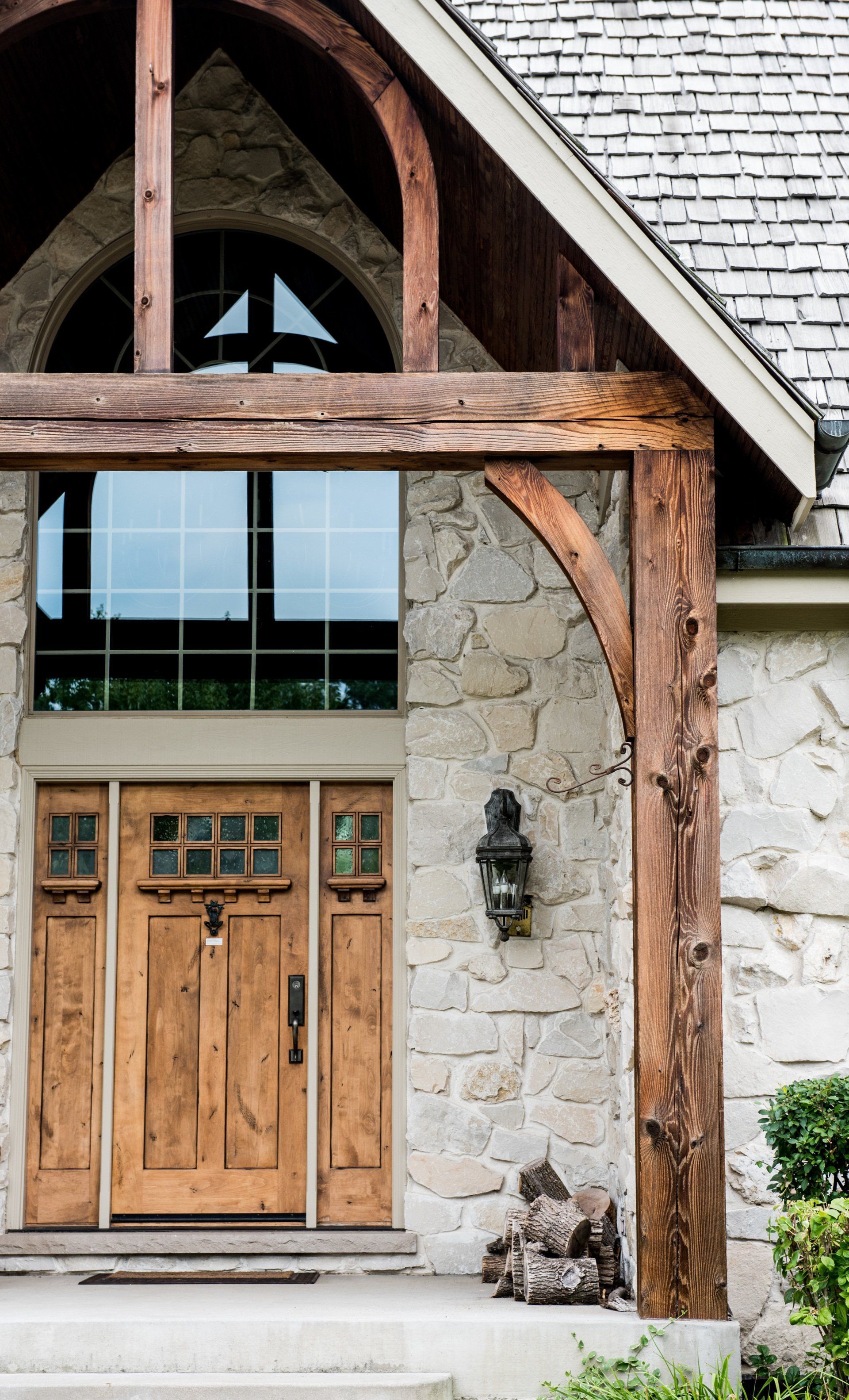 Wooden front door and rustic stone house entrance with arched timber frame and window above
