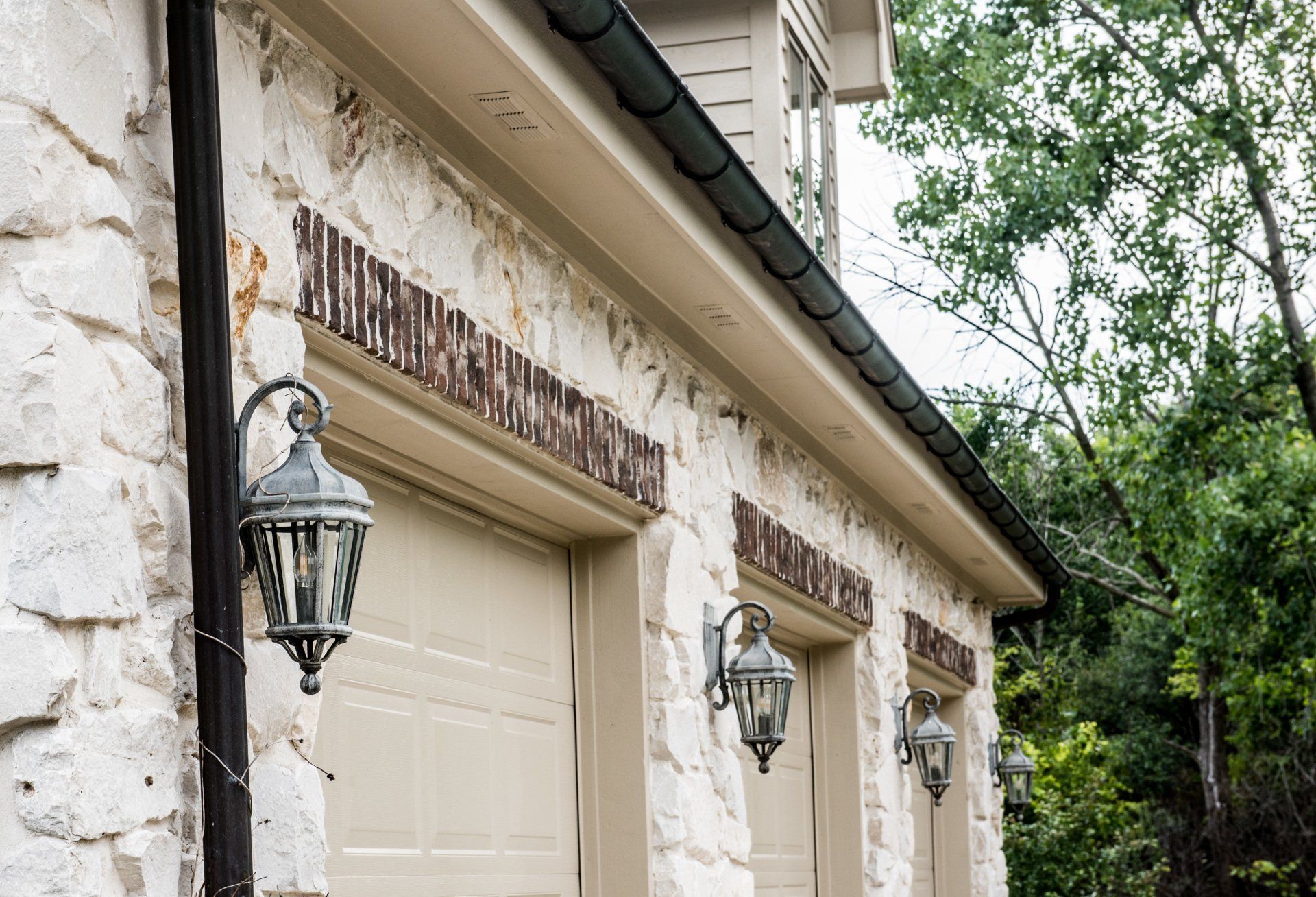 Exterior of a house with cream garage doors, stone wall, and hanging lanterns under the roofline.
