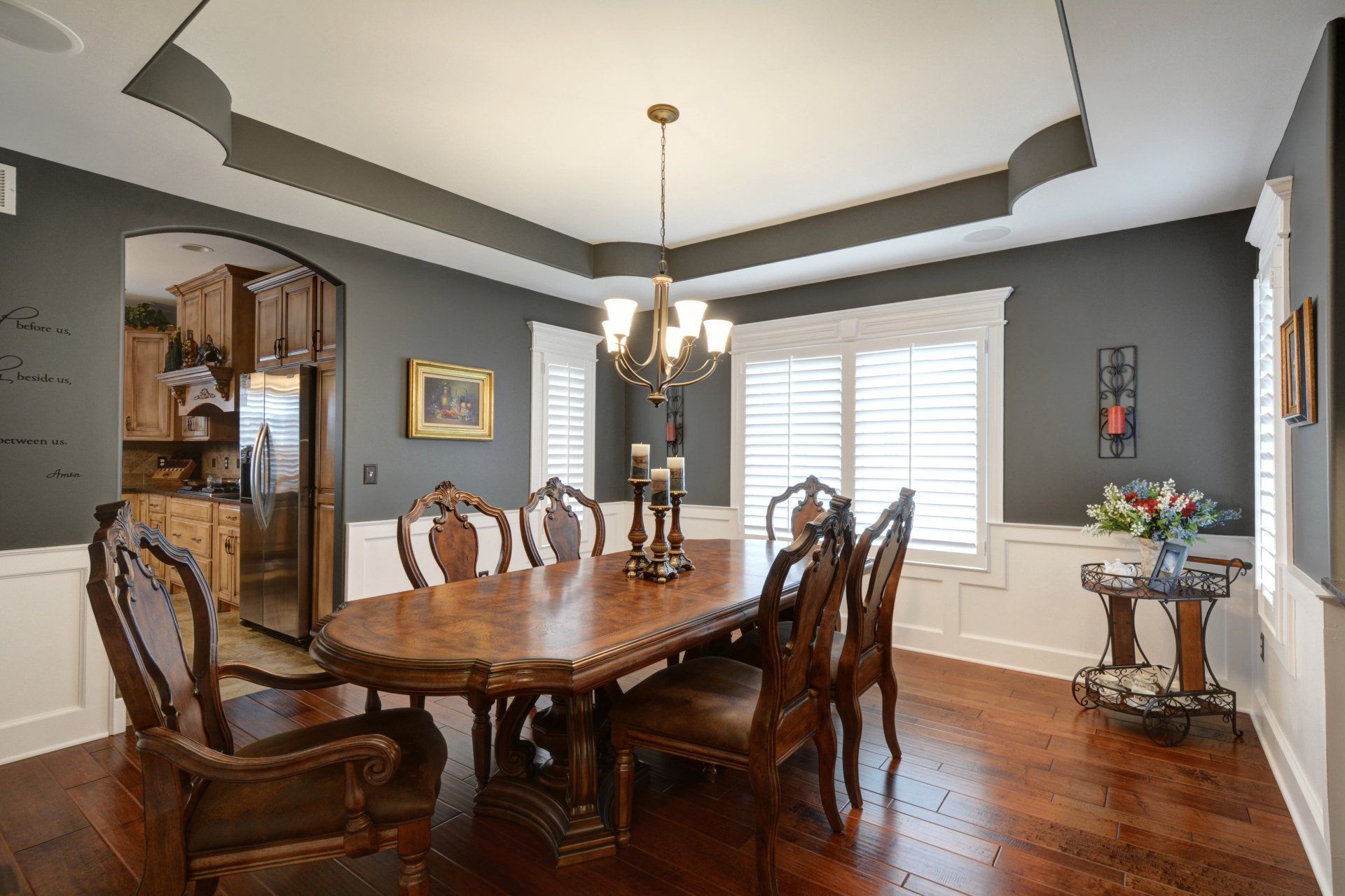 Elegant dining room with a dark wood table, chandelier, hardwood floors, and large windows with shutters