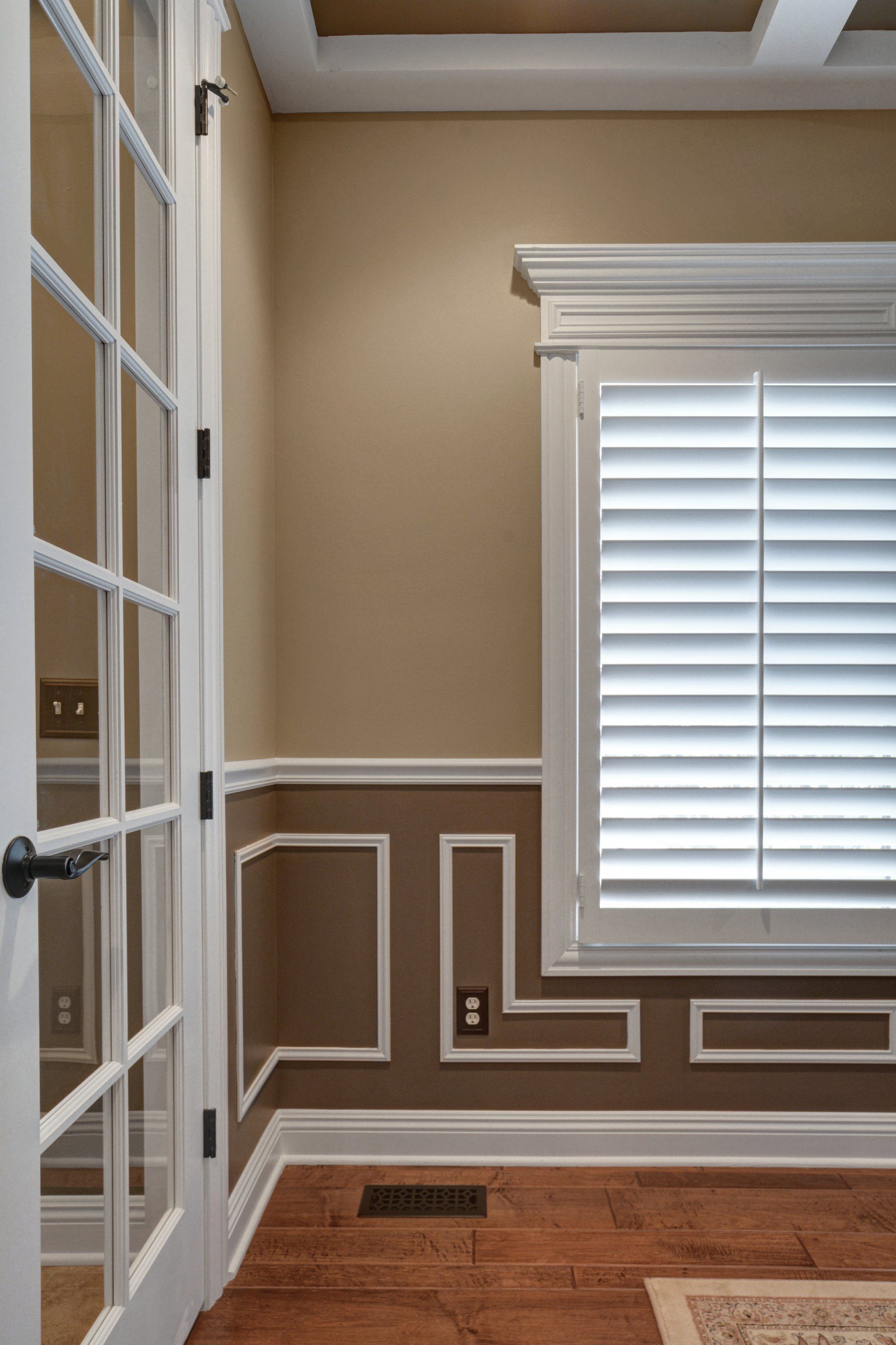 Empty room with white trim, tan walls, hardwood floor, and a window with white blinds.