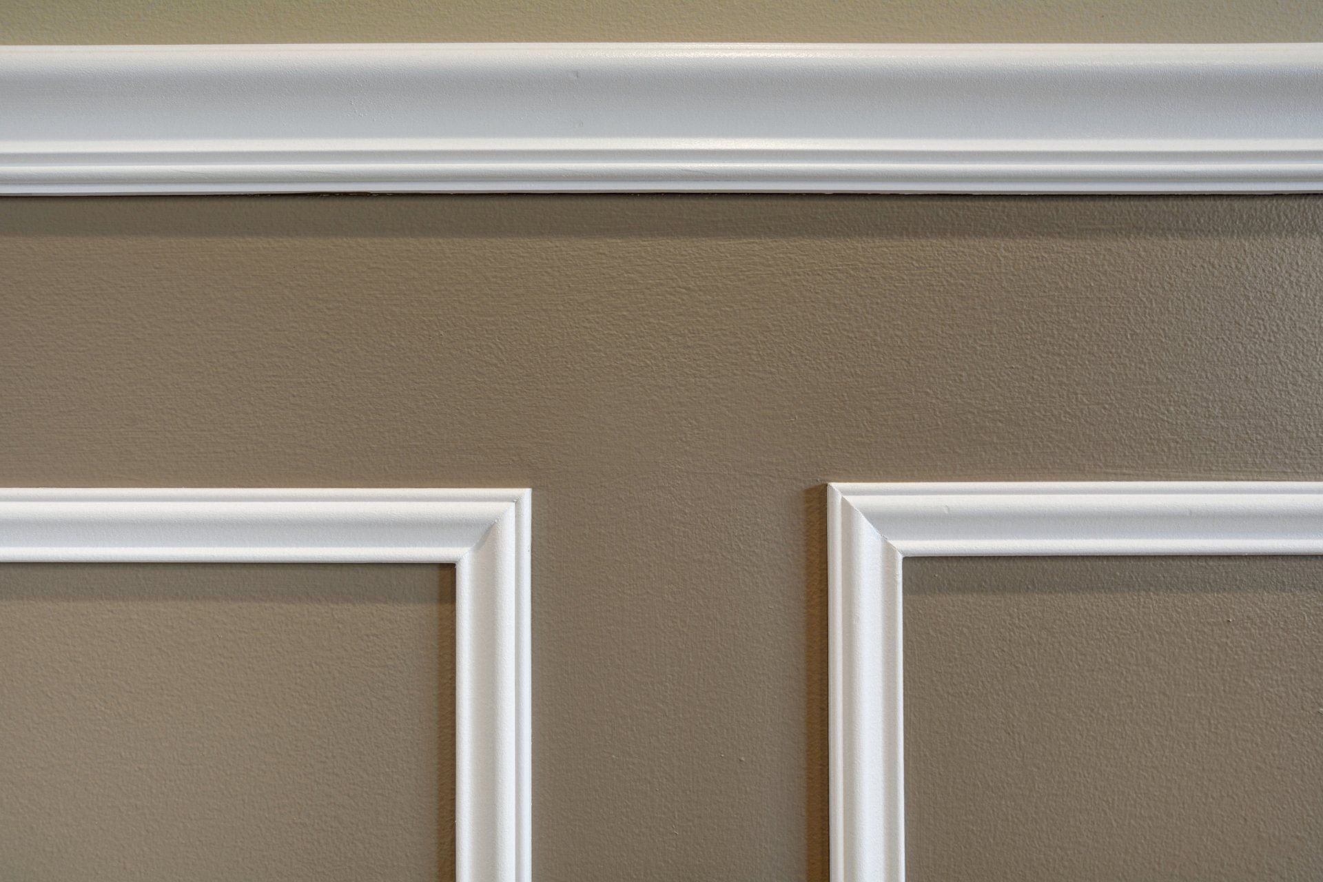 White trim molding on a beige wall near the ceiling