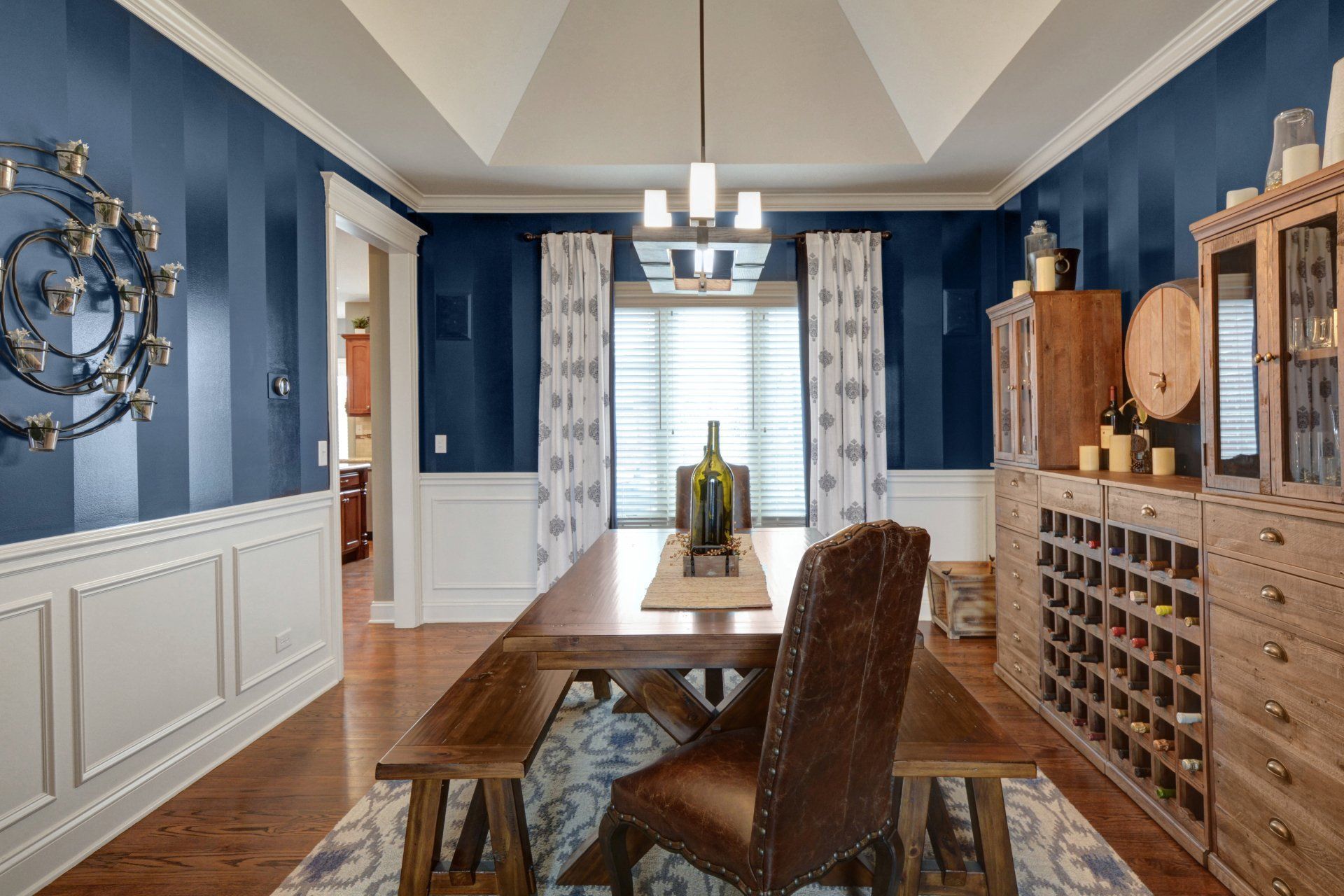Elegant dining room with blue walls, wood table, patterned chairs, and wine storage cabinetry
