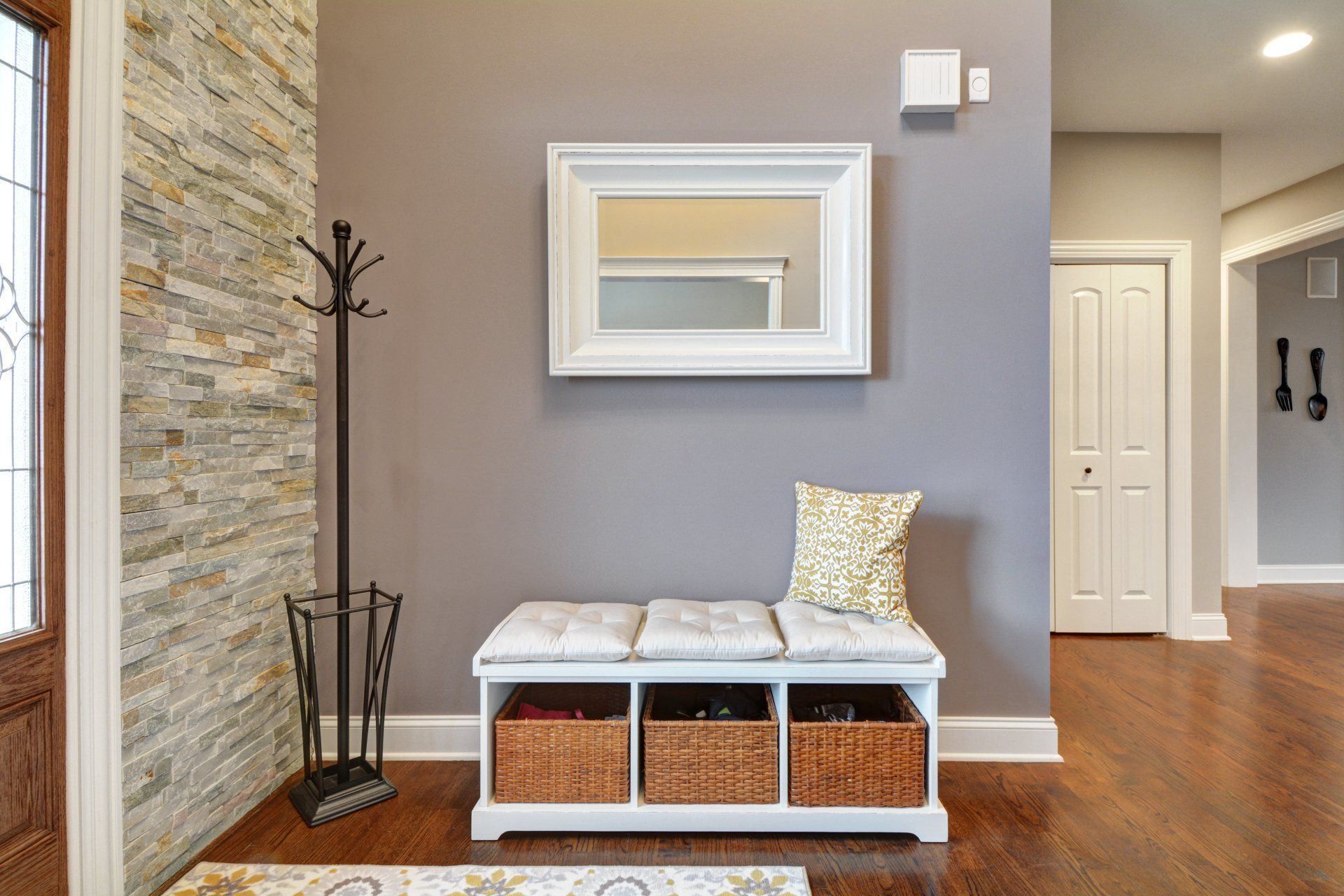 Entryway bench with baskets, coat rack, mirror, and hardwood floor in a modern home foyer