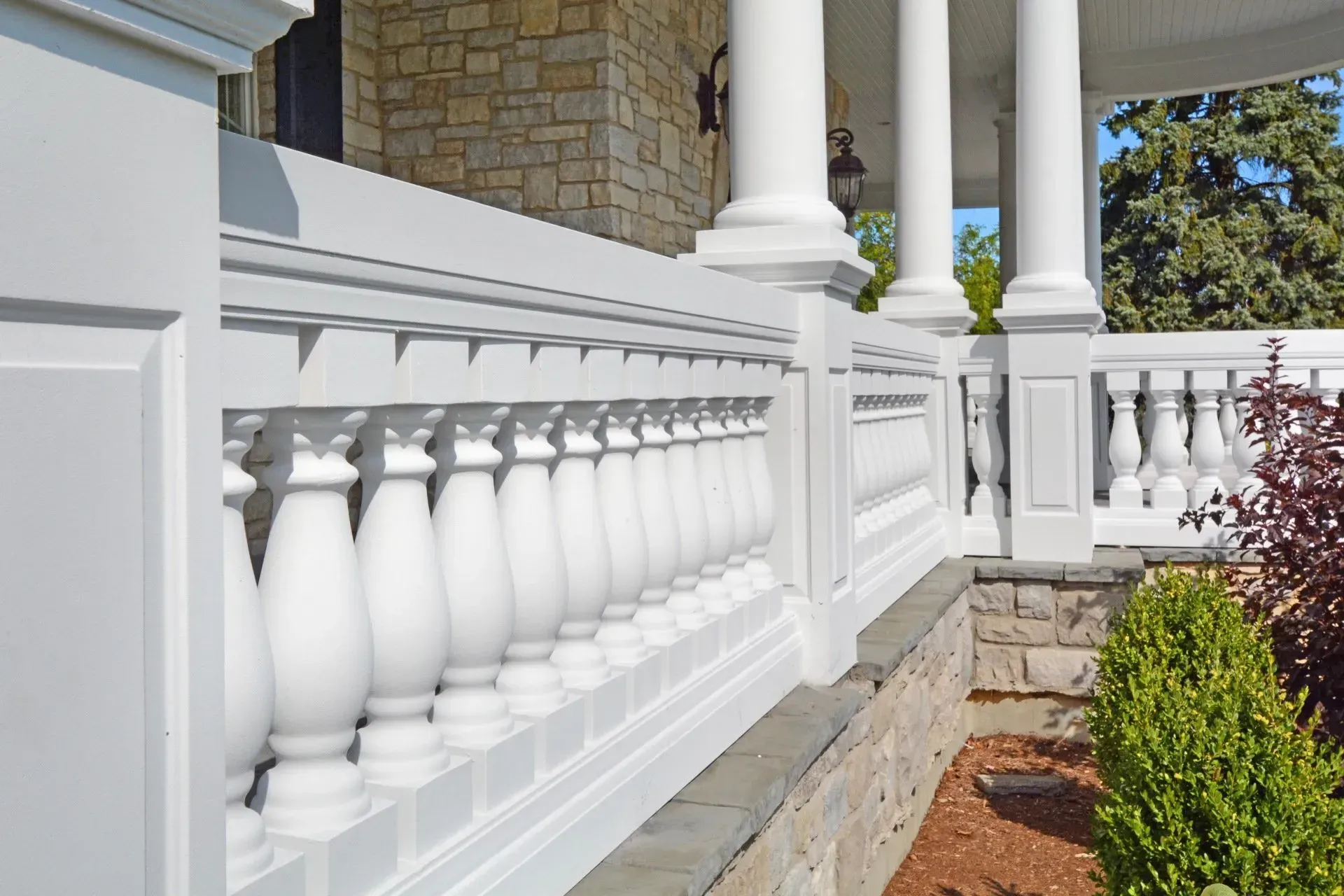 White porch railing and stone columns beside a landscaped front walkway