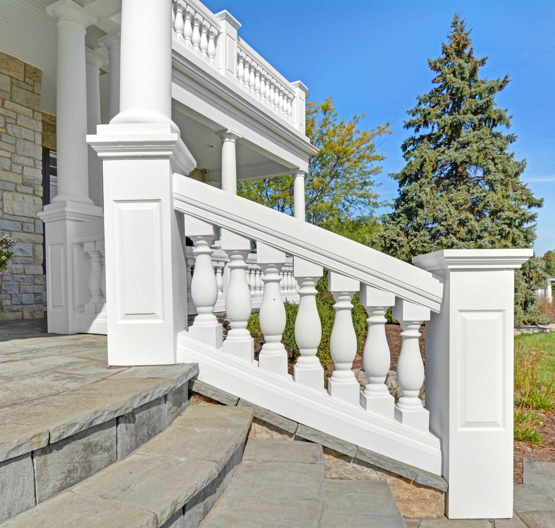 White stone porch railing and steps on a house exterior under a clear blue sky
