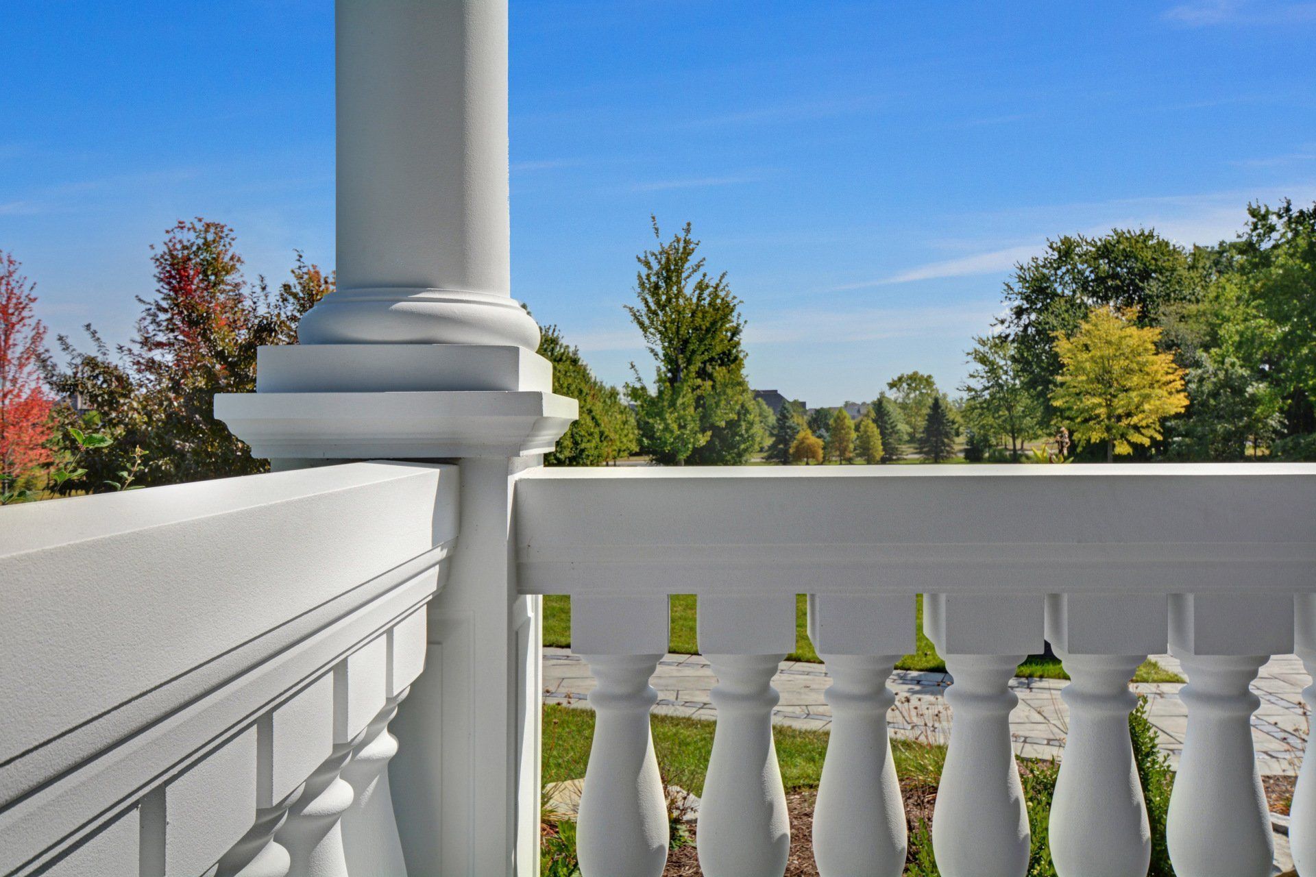 White porch with balustrade, column, and autumn trees under a clear blue sky