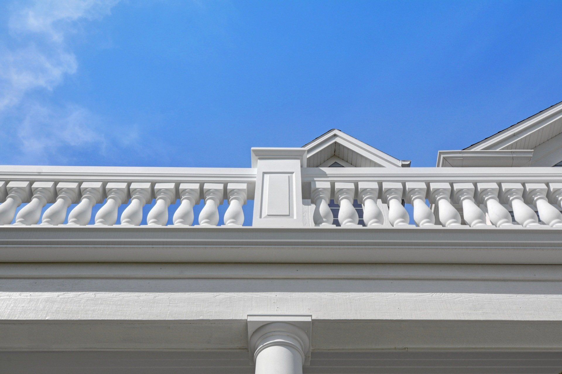 White building facade with balcony balusters and a central decorative pediment against a blue sky