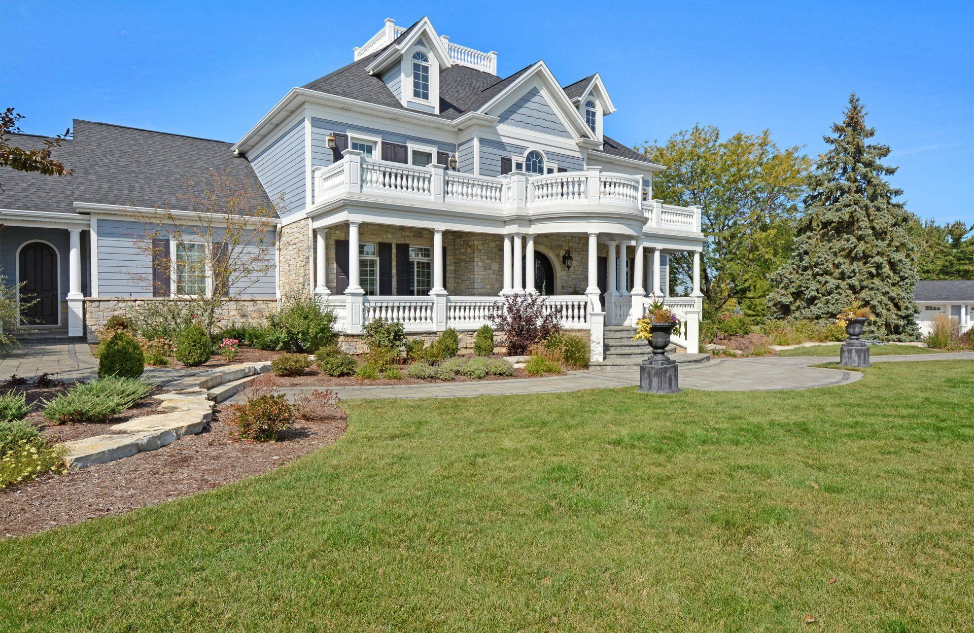 Large gray Victorian-style house with white trim, wraparound porch, and landscaped lawn