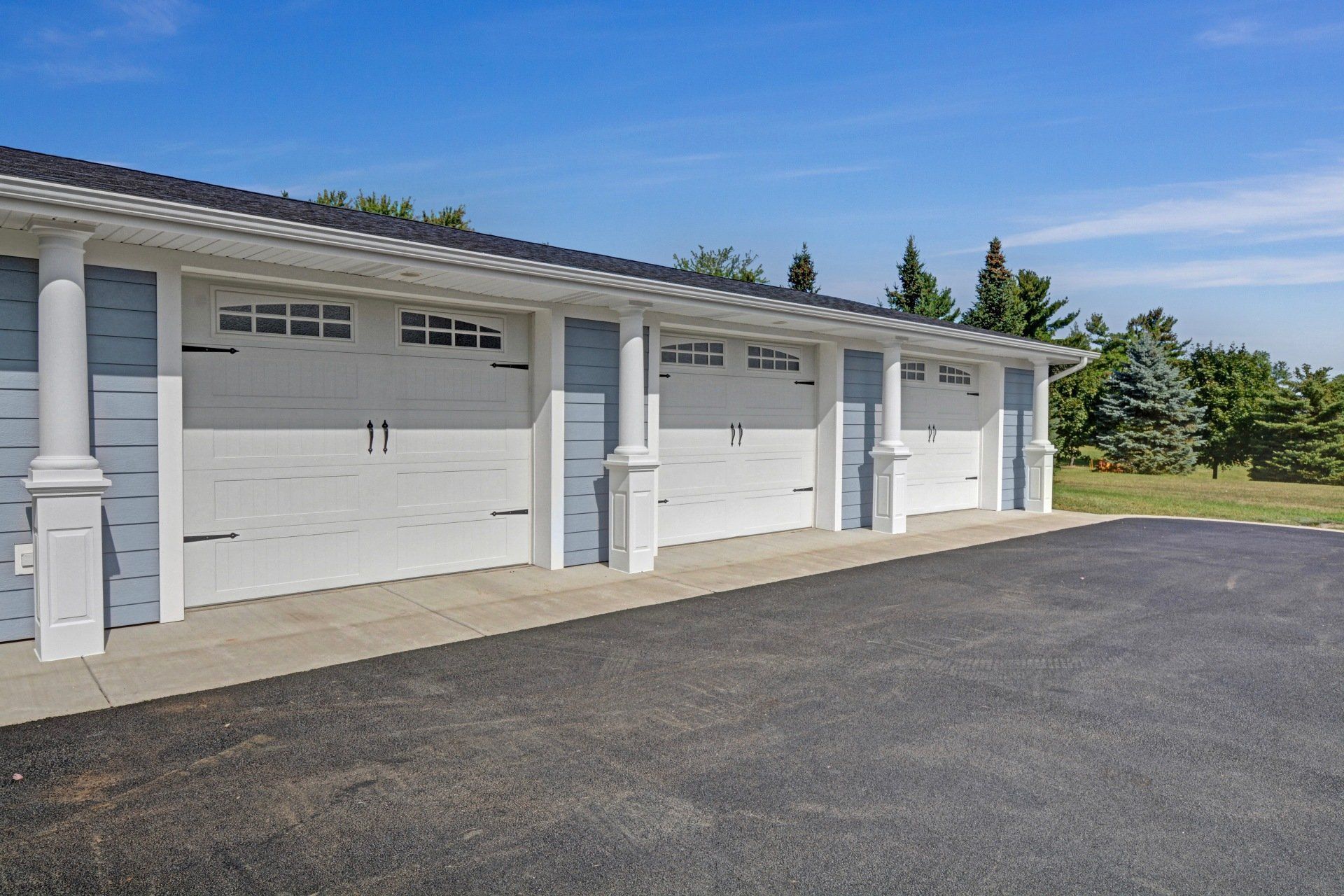 Row of white garage doors on a sunny suburban driveway beside green trees