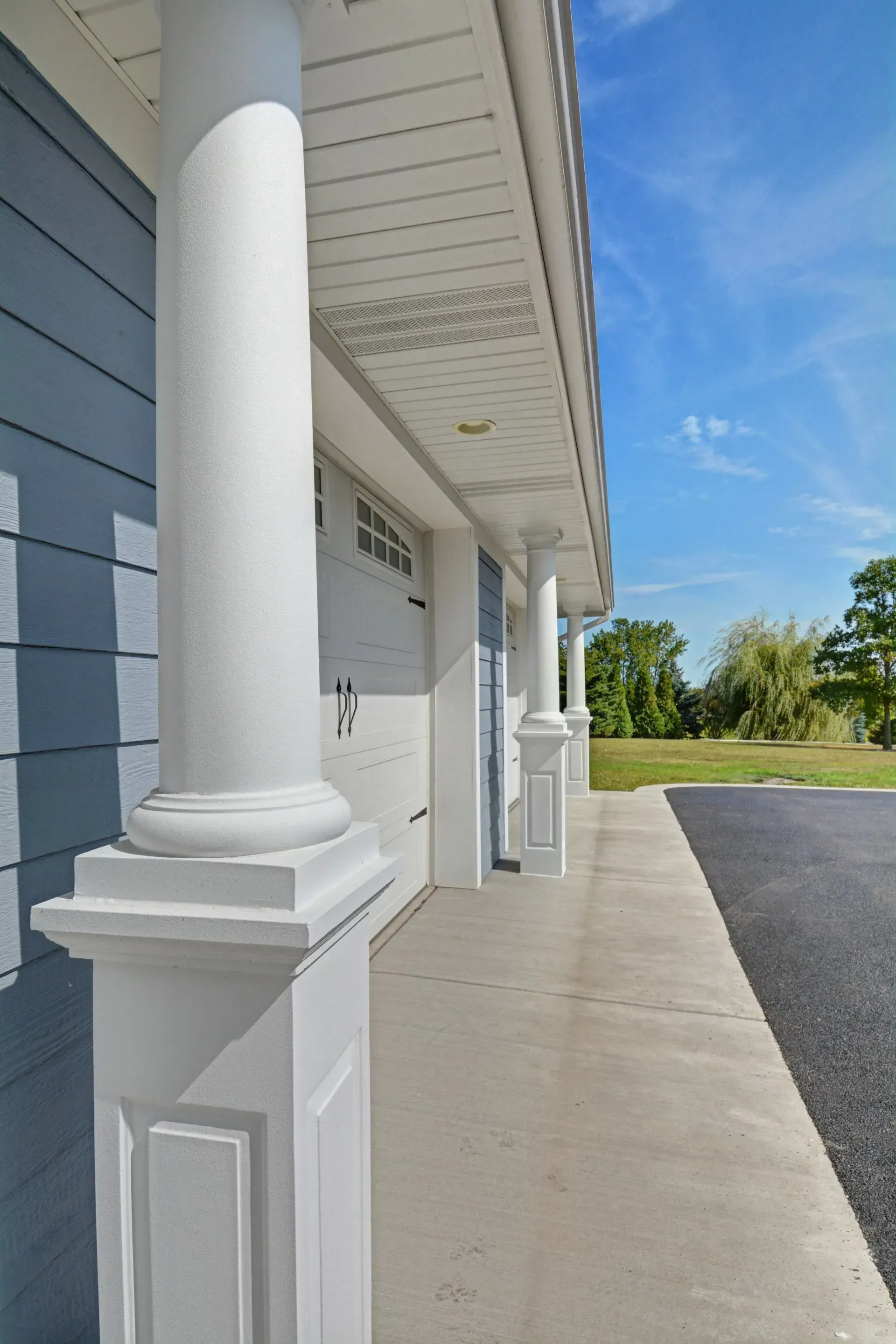 White house porch with columns and concrete walkway beside a gravel driveway under a blue sky