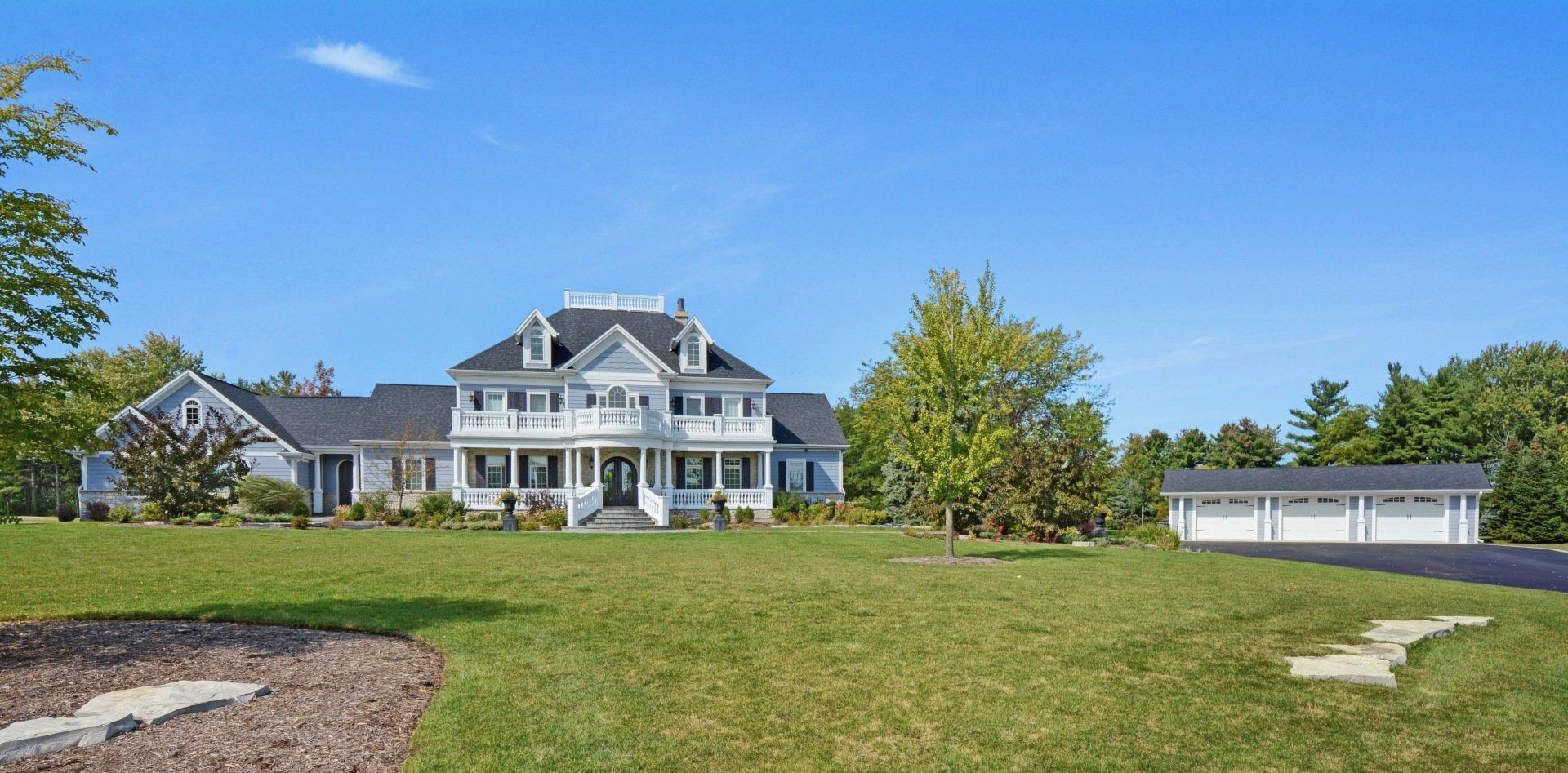 Large white house with blue shutters on a grassy hill under a clear blue sky
