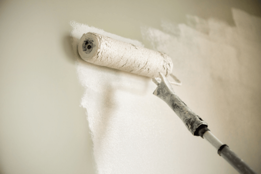 Paint roller applying white paint to a wall indoors