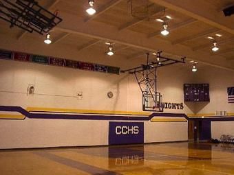 Empty high school gym with polished floor, white walls, and basketball hoops overhead