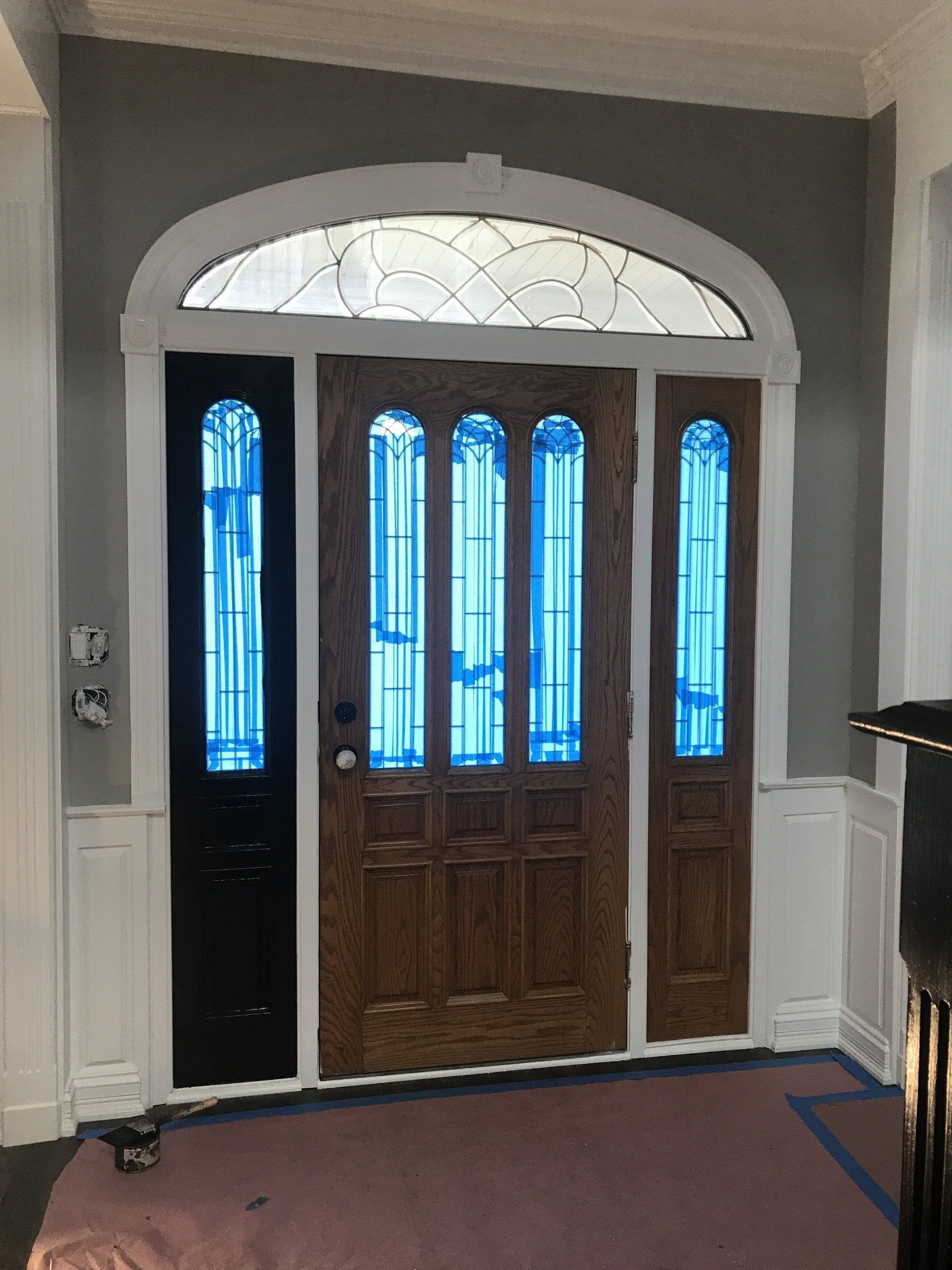 Front entry door with stained glass panels and arched transom in a gray-and-white hallway