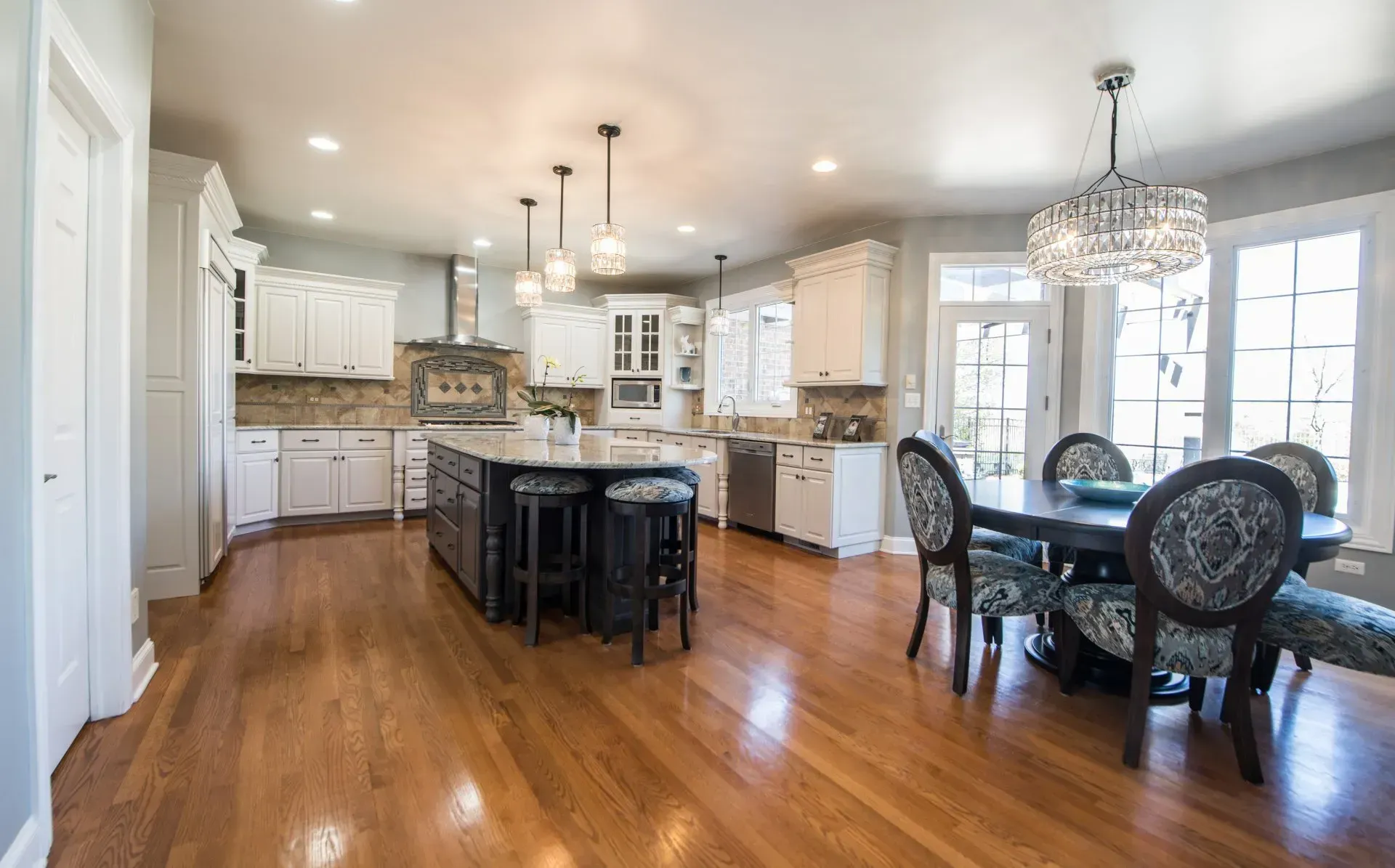 Bright open kitchen and dining area with hardwood floors, white cabinetry, island, and chandelier lighting