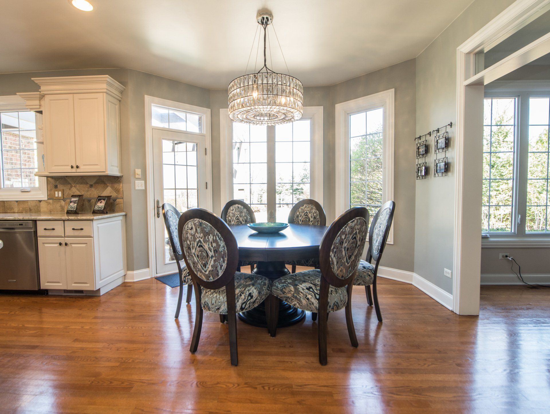 Bright dining room with round table, chandelier, hardwood floors, and large windows.