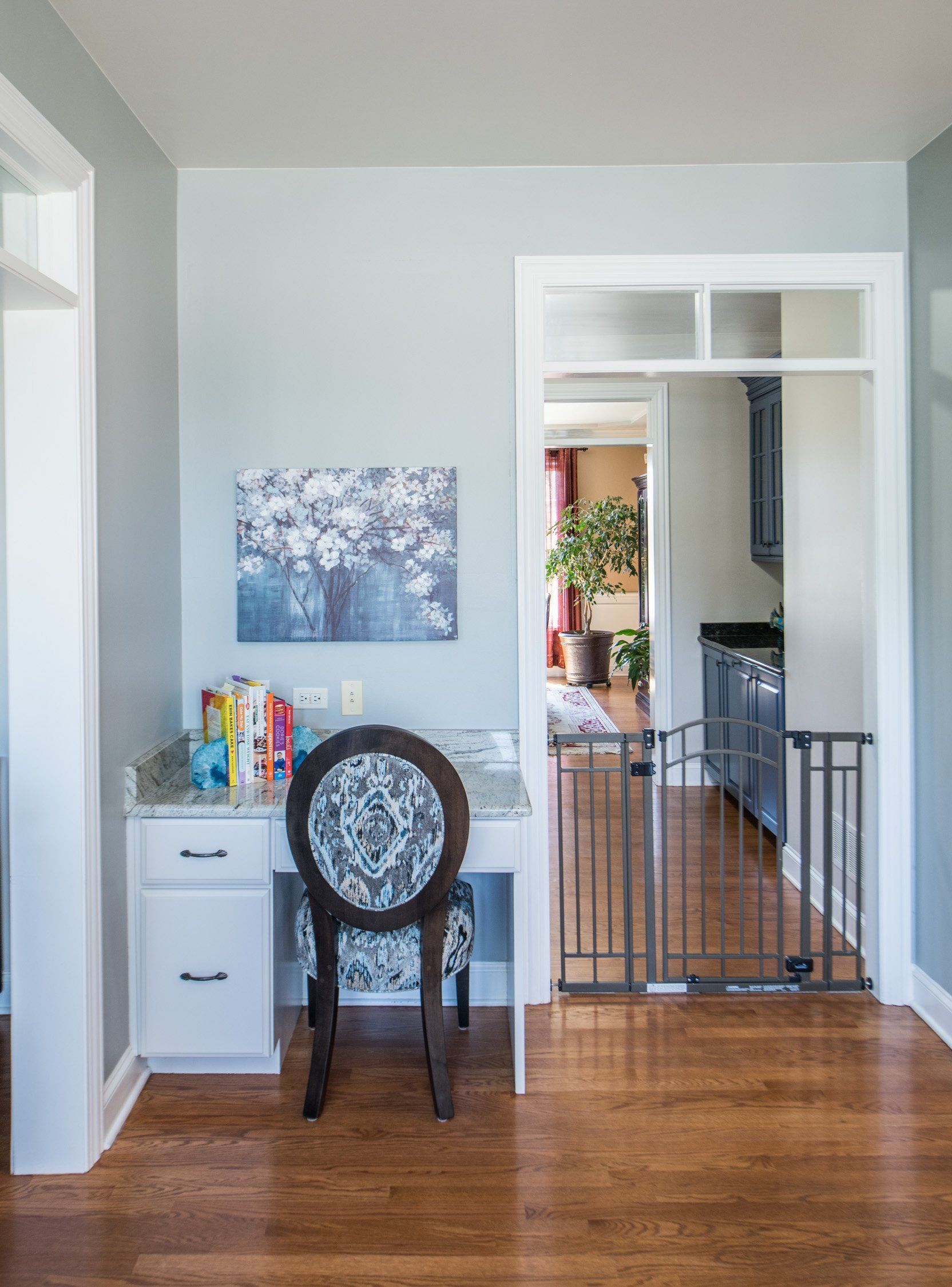 Small home office with a desk, ornate chair, and wall art in a hardwood-floored hallway.