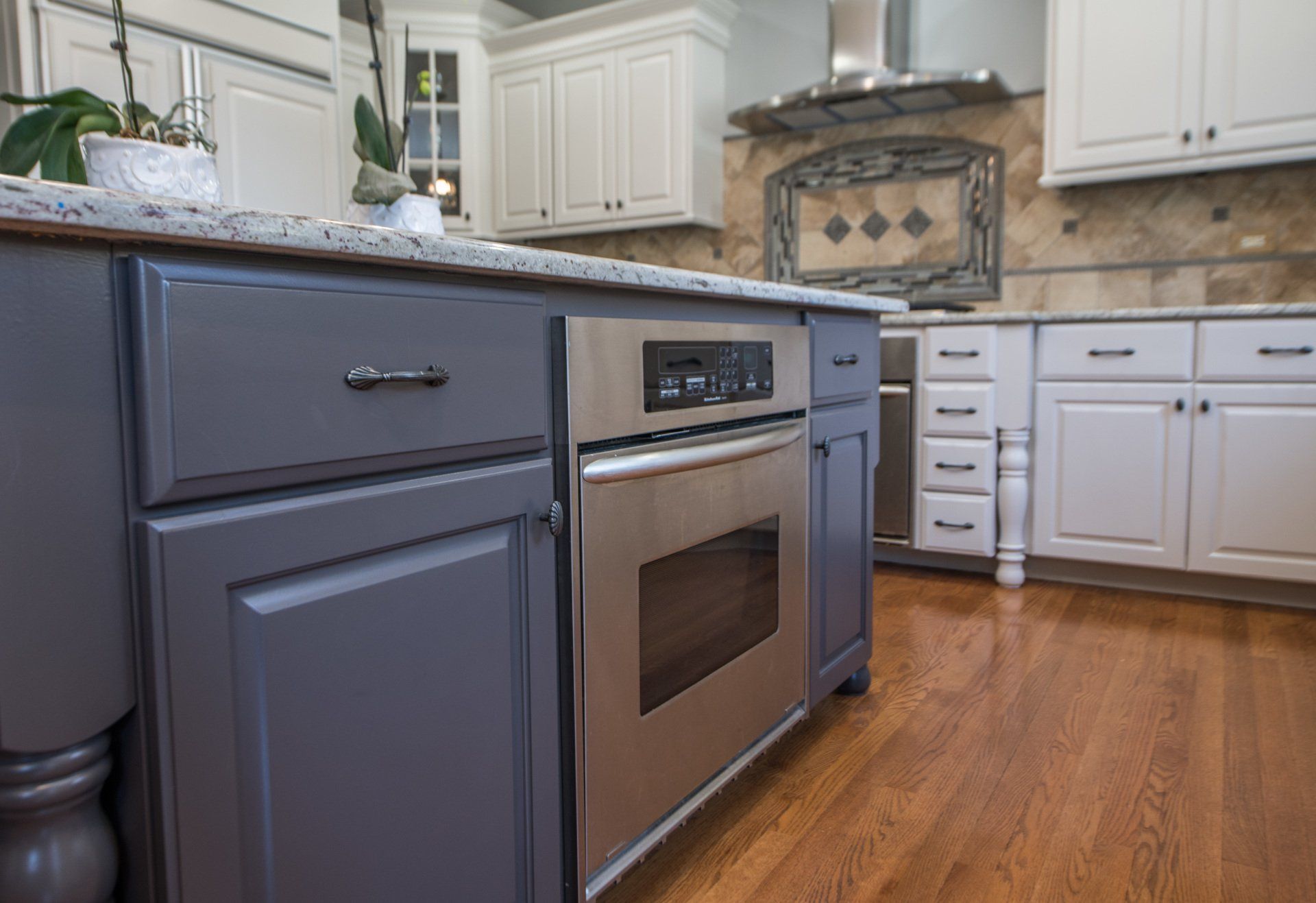 Modern kitchen with gray cabinets, stainless steel oven, white countertops, and hardwood floor