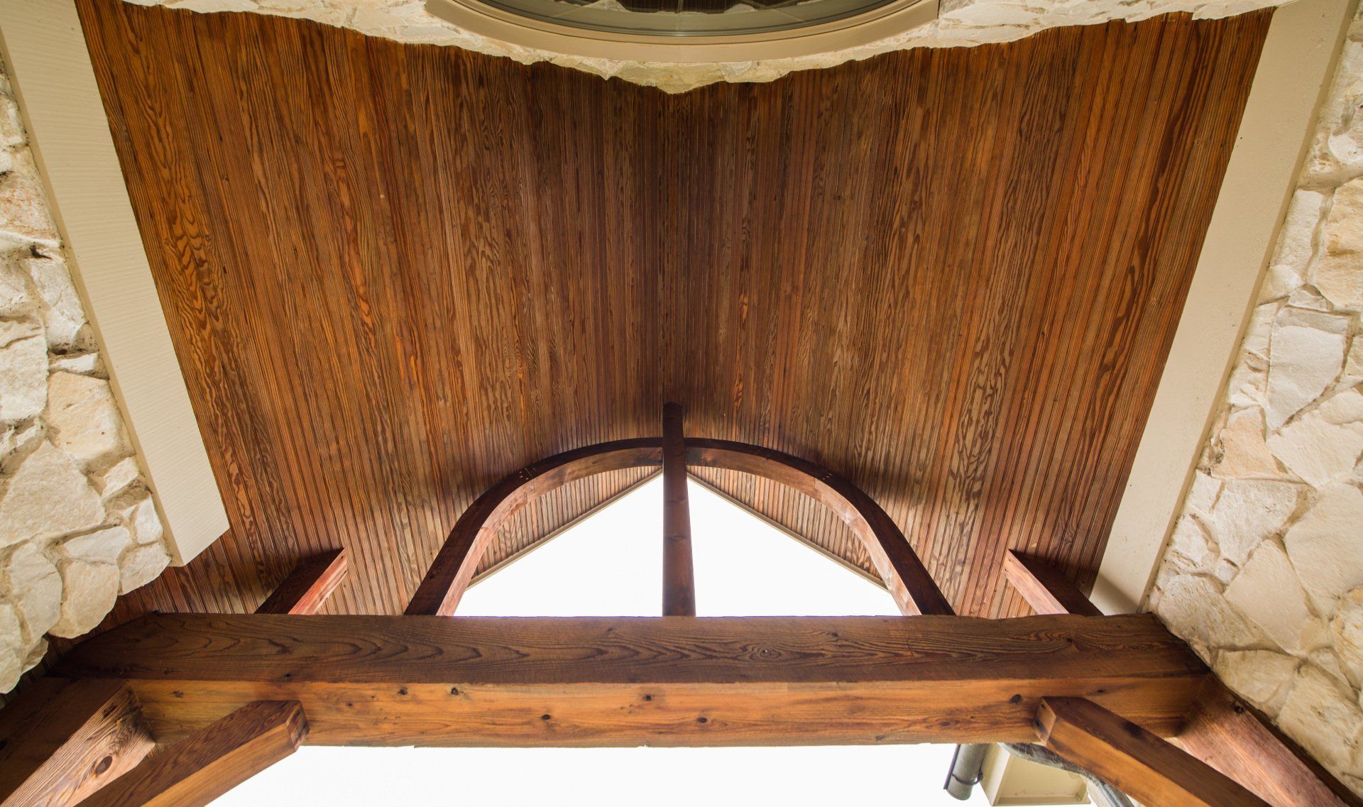 Wooden vaulted ceiling with arched window and stone walls in a rustic interior