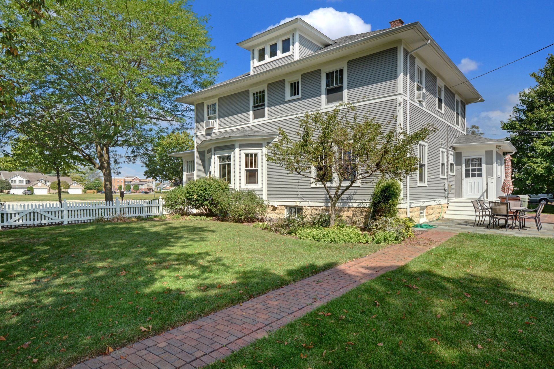 Gray two-story house with a front lawn, brick walkway, and blue sky