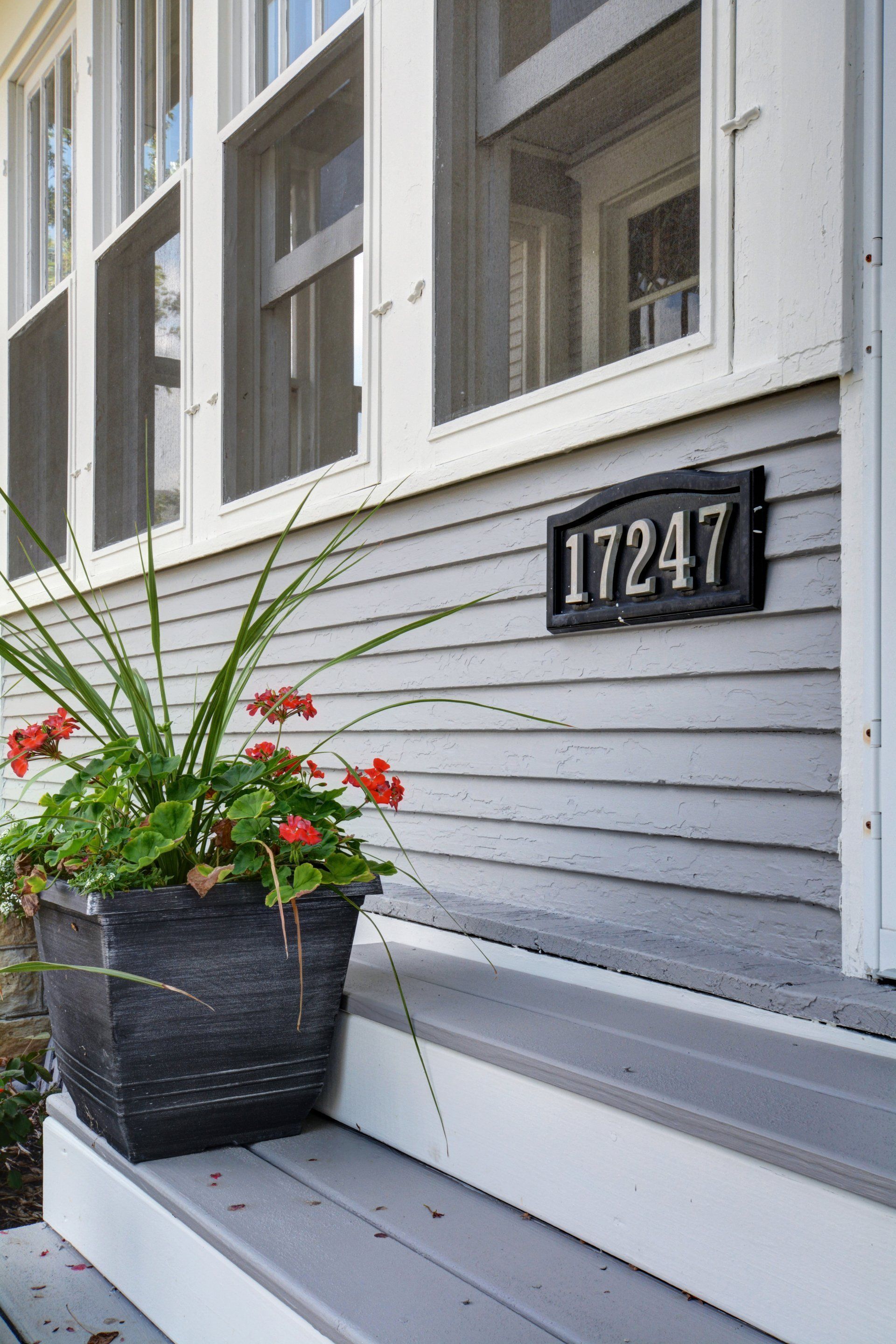 Front porch with black planter of red flowers and house number 17247 beside white siding and windows