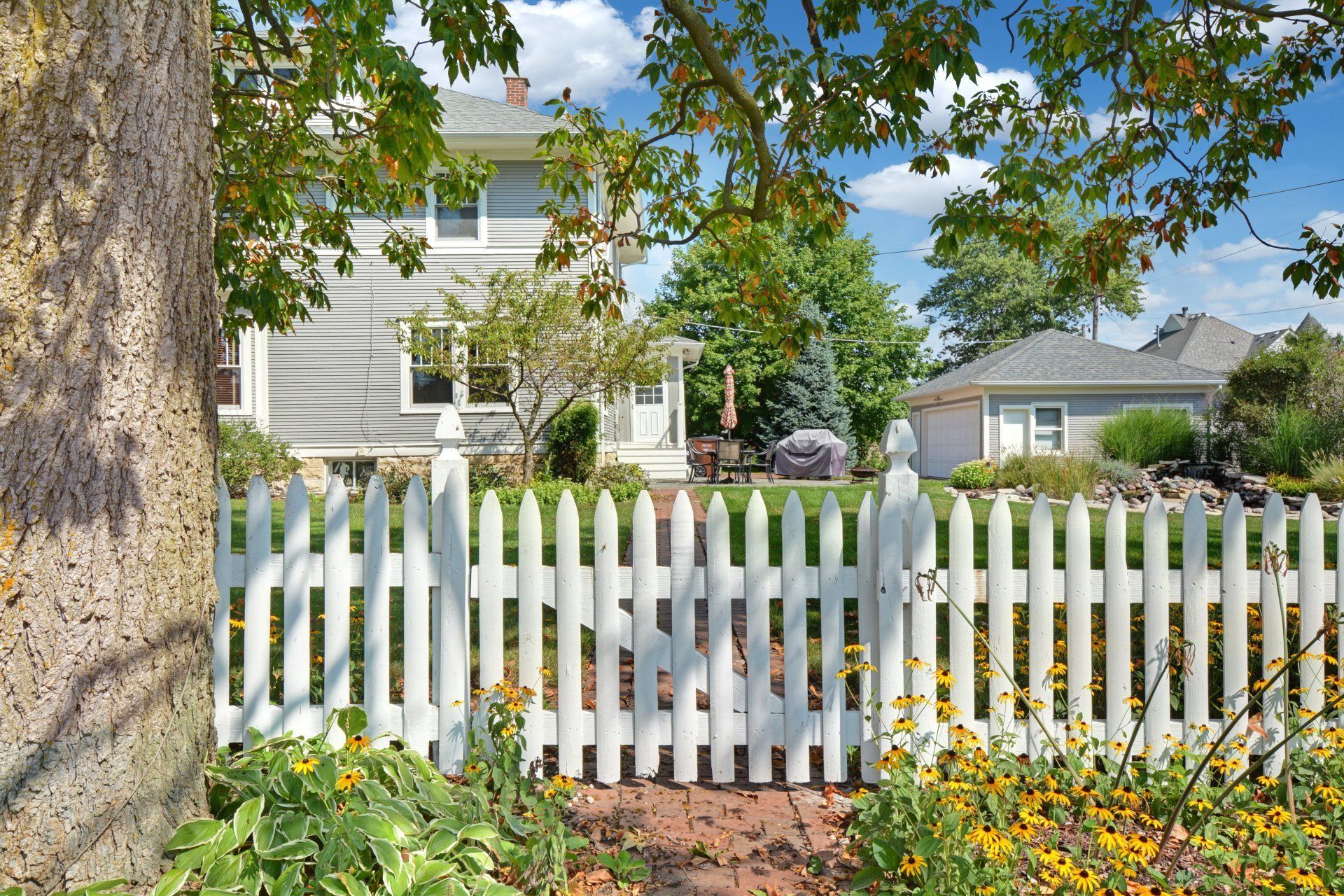 White picket fence in a leafy suburban garden with a gray house in the background
