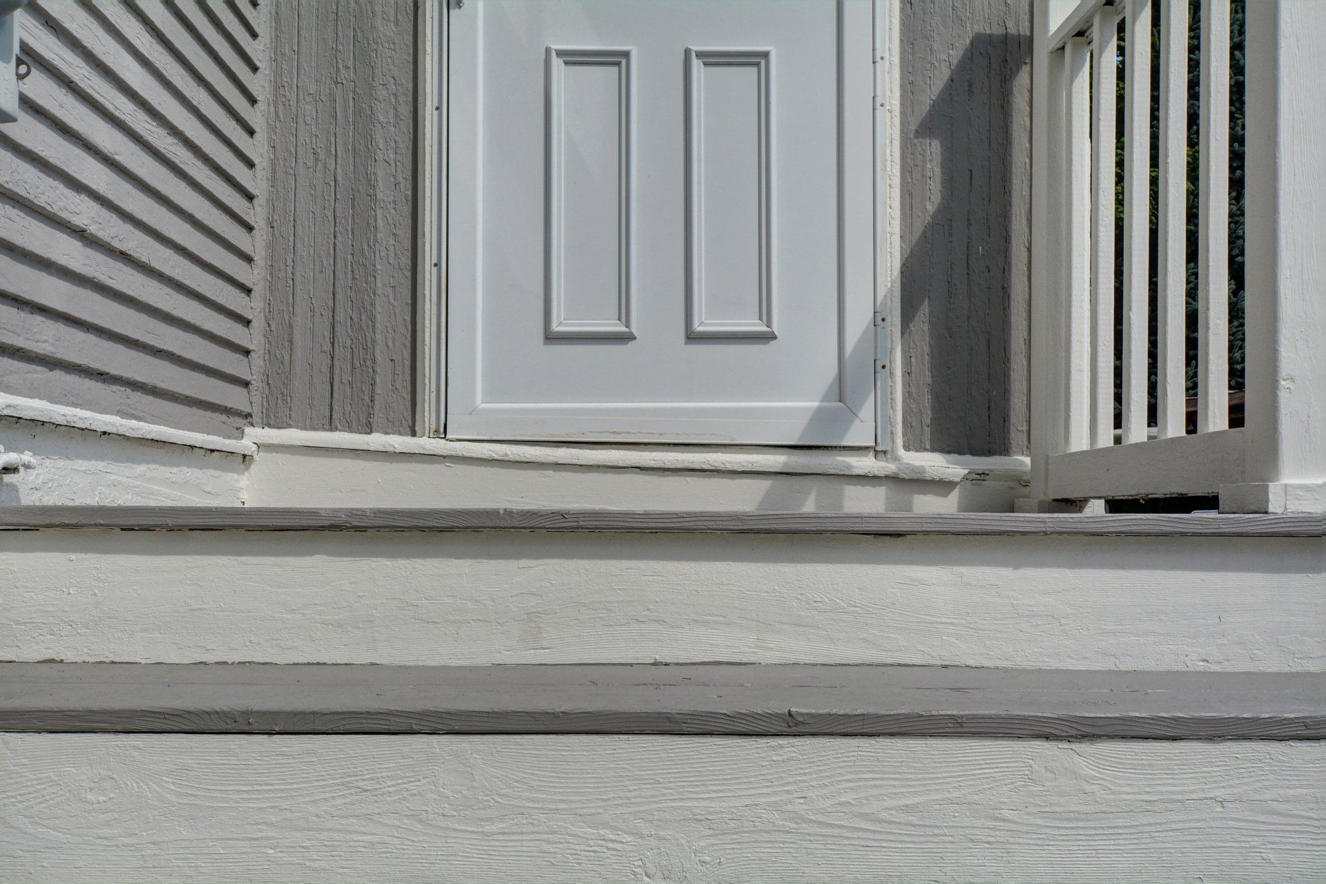 Front porch steps leading to a white front door with gray siding and railings