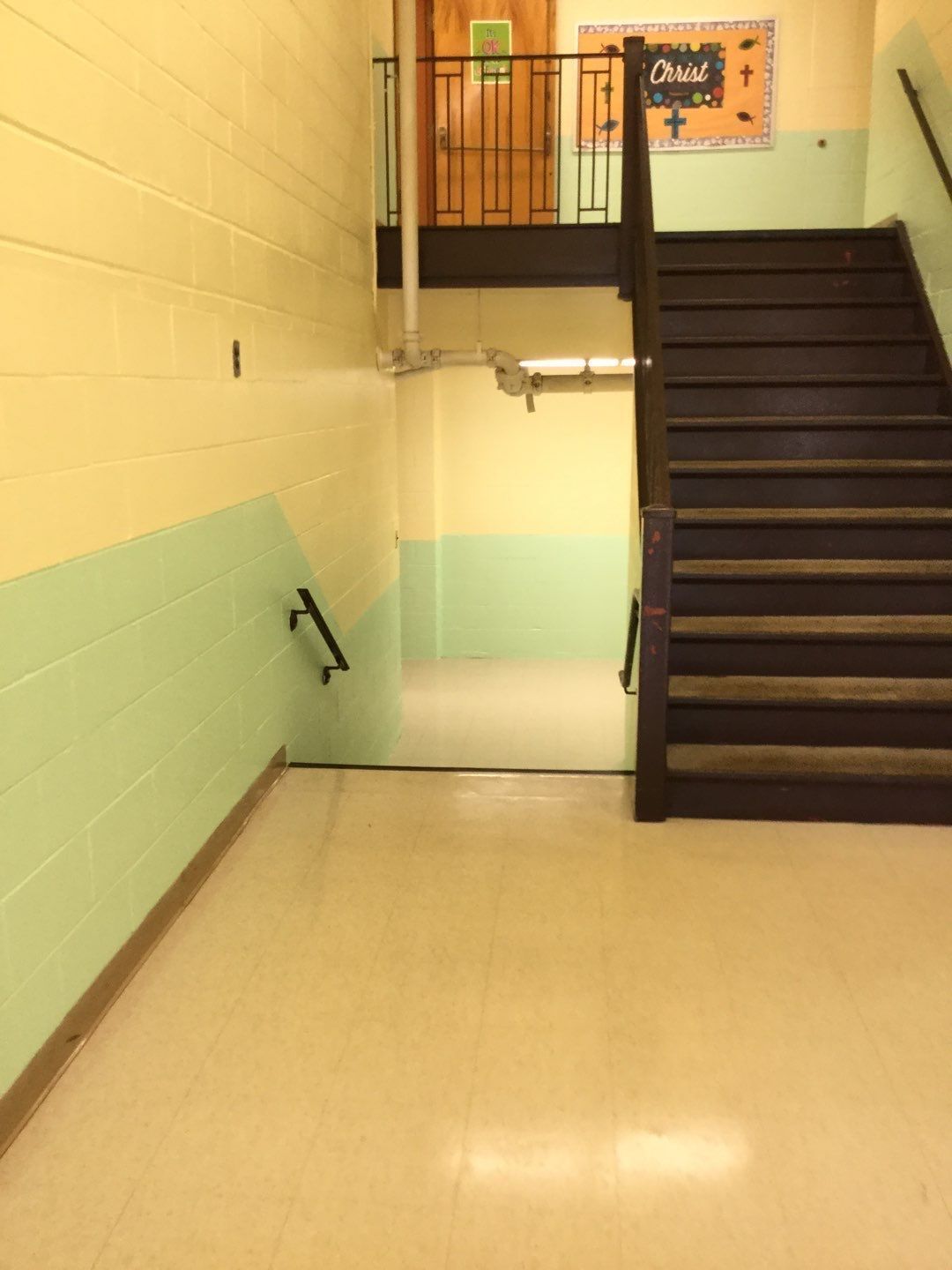 Empty school stairwell with dark stairs, handrails, and pale yellow-green walls.