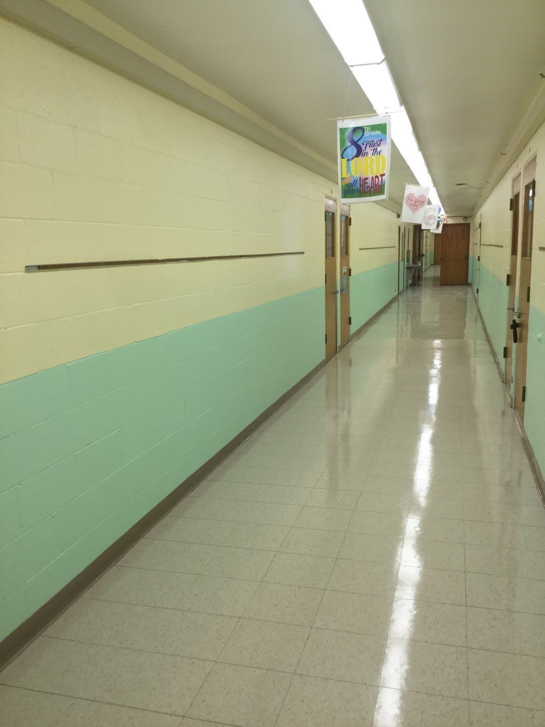 Empty school hallway with beige and mint green walls, glossy floor, and posters overhead