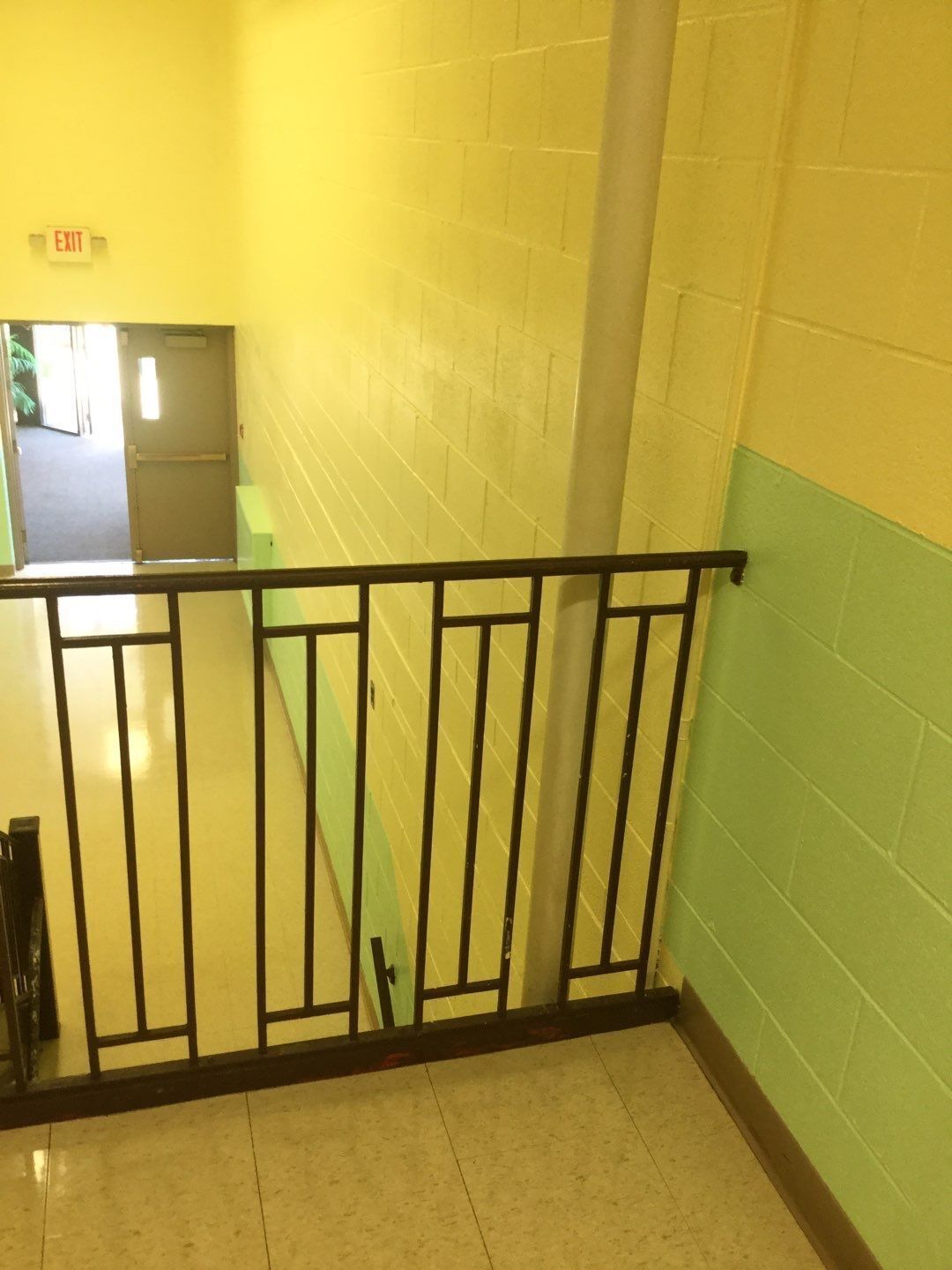Indoor stairwell with black railing, yellow walls, and a green lower wall near a doorway below.