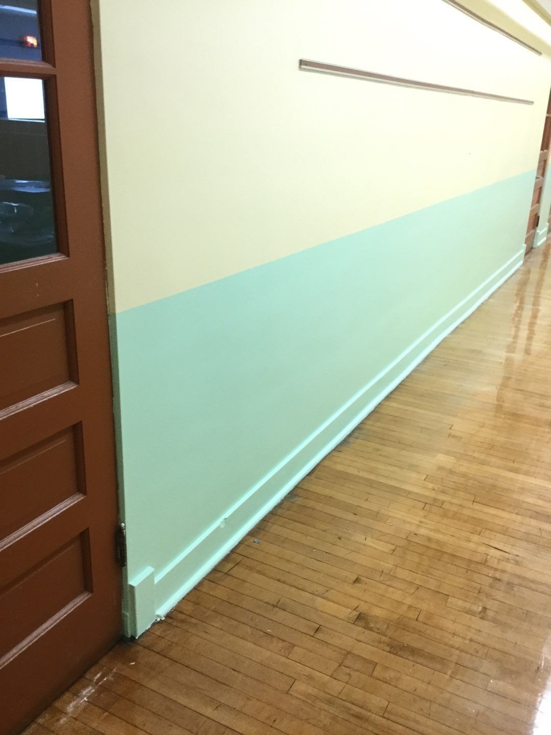 Hallway with mint and cream walls, wooden floor, and a brown door on the left.