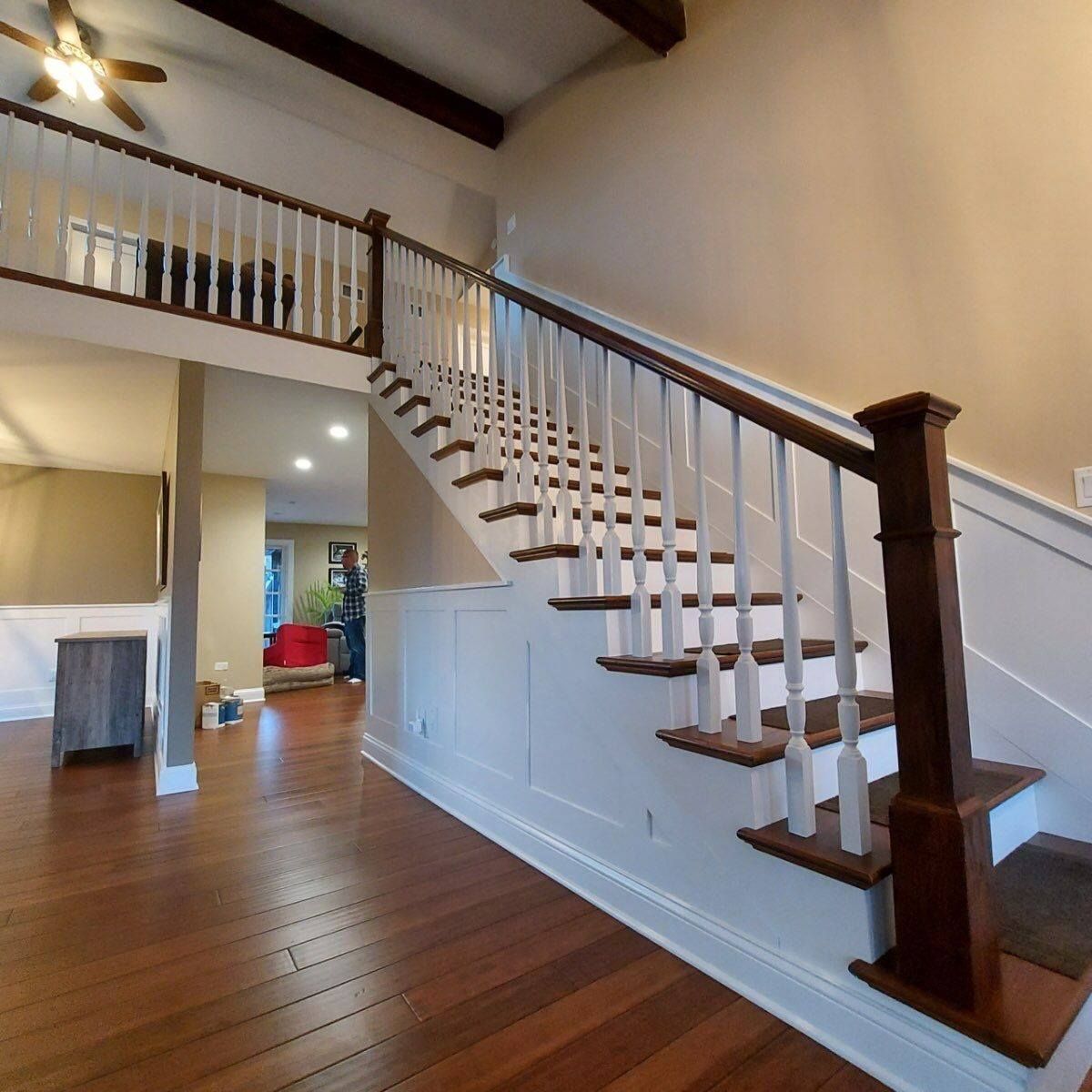 Interior foyer with hardwood floors and a white staircase with dark wood railing leading to an upstairs balcony.
