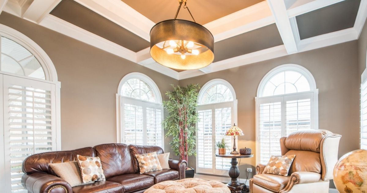 Bright living room with arched windows, leather sofa, recliner, and a vaulted ceiling with a chandelier