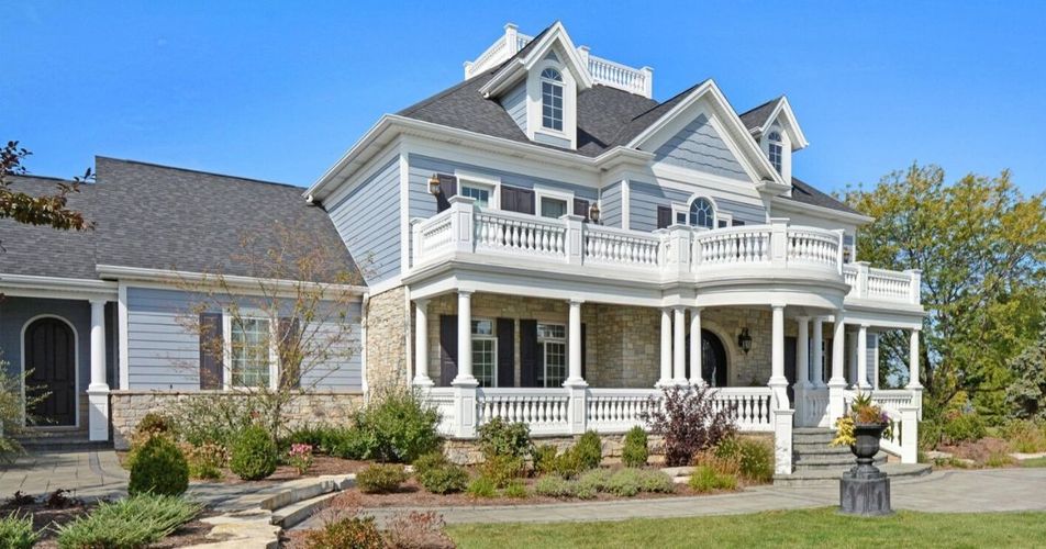 Victorian-style white house with a porch, balcony, and dormer windows on a sunny day