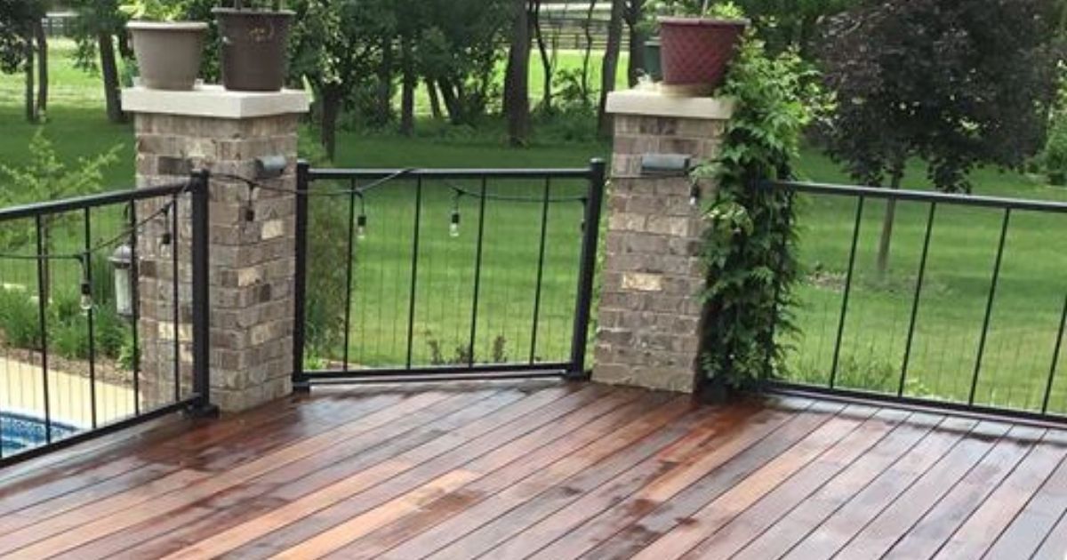 Wet wooden deck with black metal railing and brick pillars overlooking a green backyard after rain
