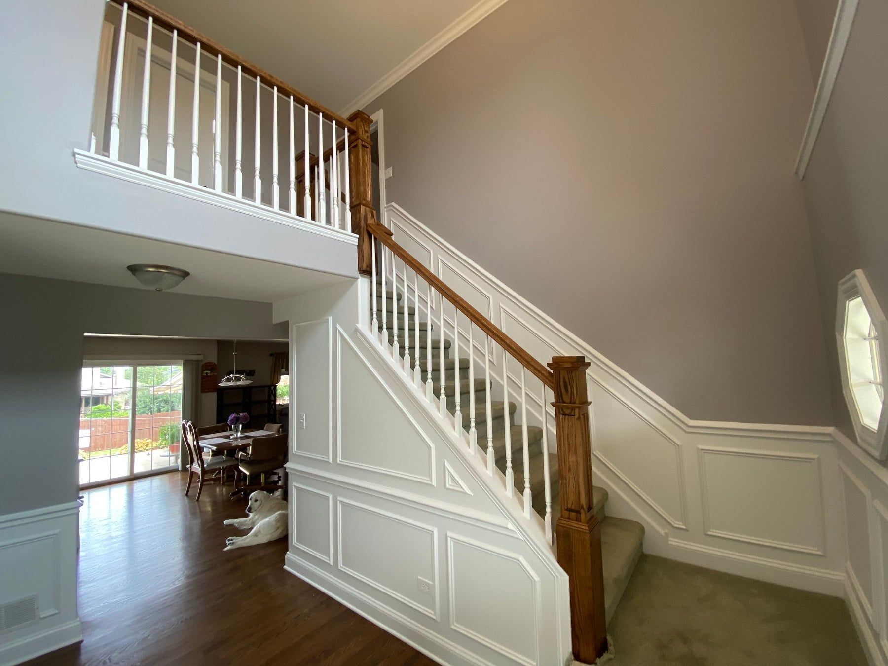 Interior staircase with white paneling, wood handrail, and loft railing in a bright entryway