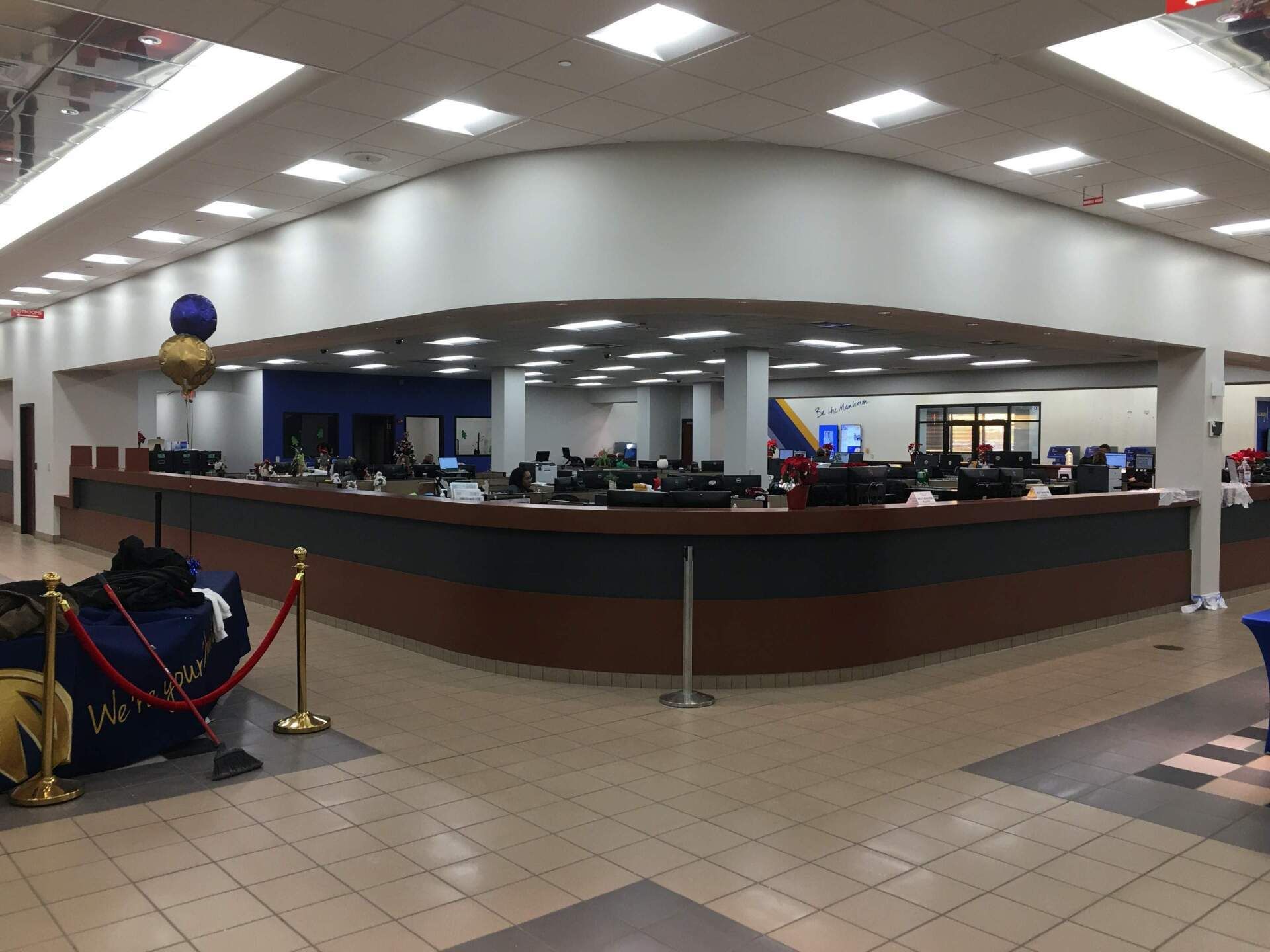 Wide indoor lobby with a long curved service desk, tiled floor, and balloon decorations under bright ceiling lights