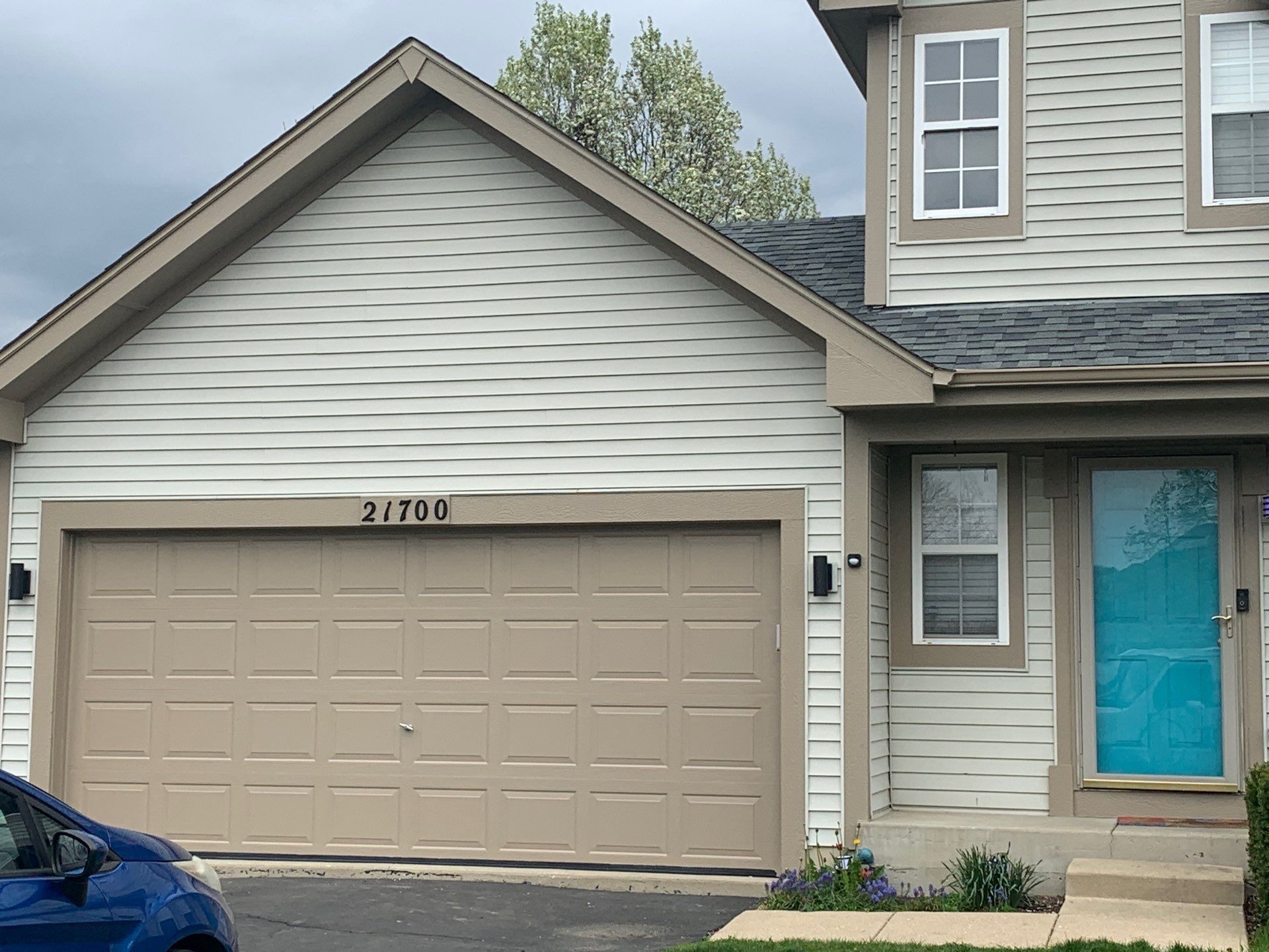 Suburban house exterior with tan garage, blue front door, and blue car partially visible