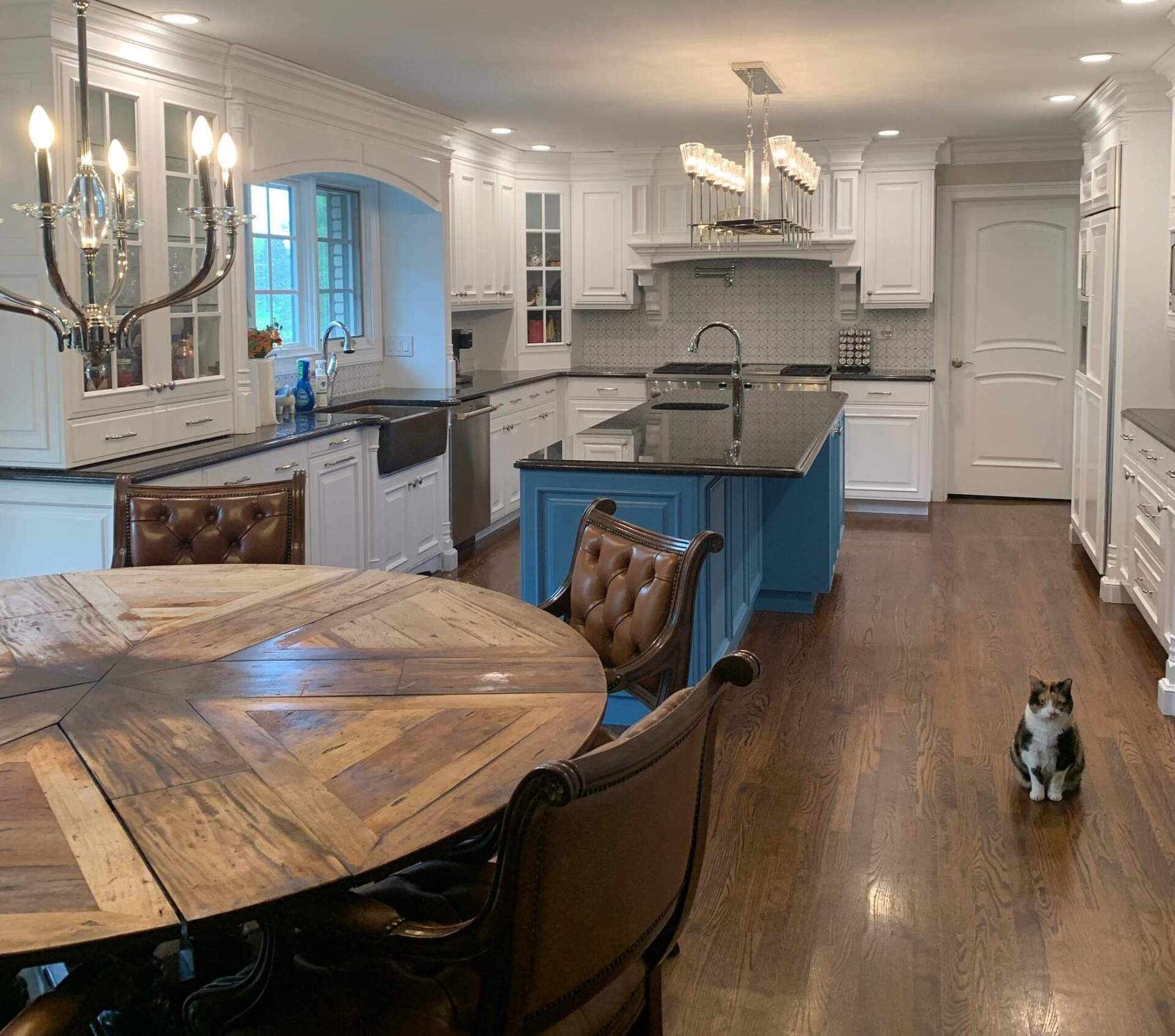 Bright white kitchen with blue island, round wooden table, and small dog on hardwood floor